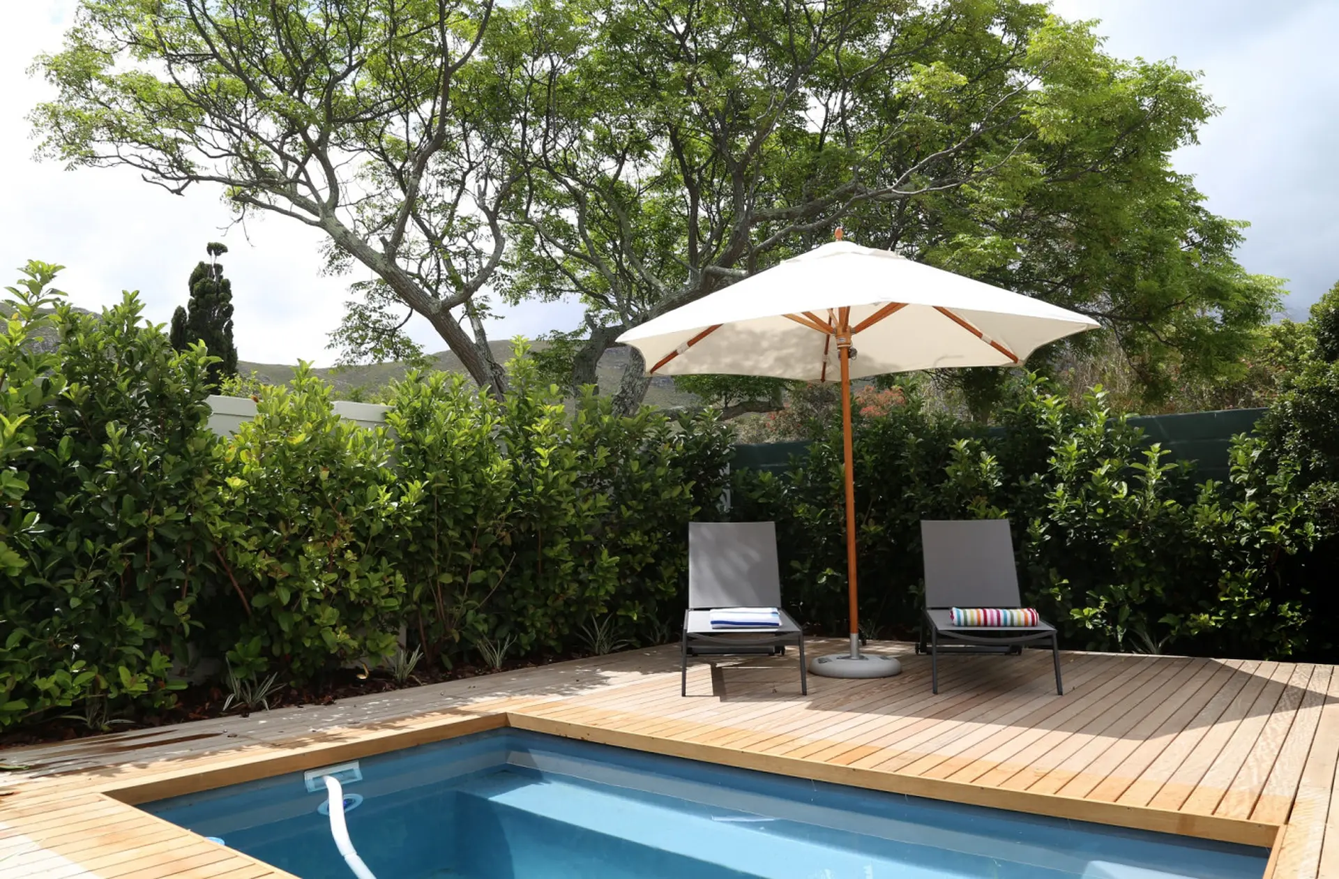 A poolside scene with a white umbrella, two lounge chairs, and a swimming pool.