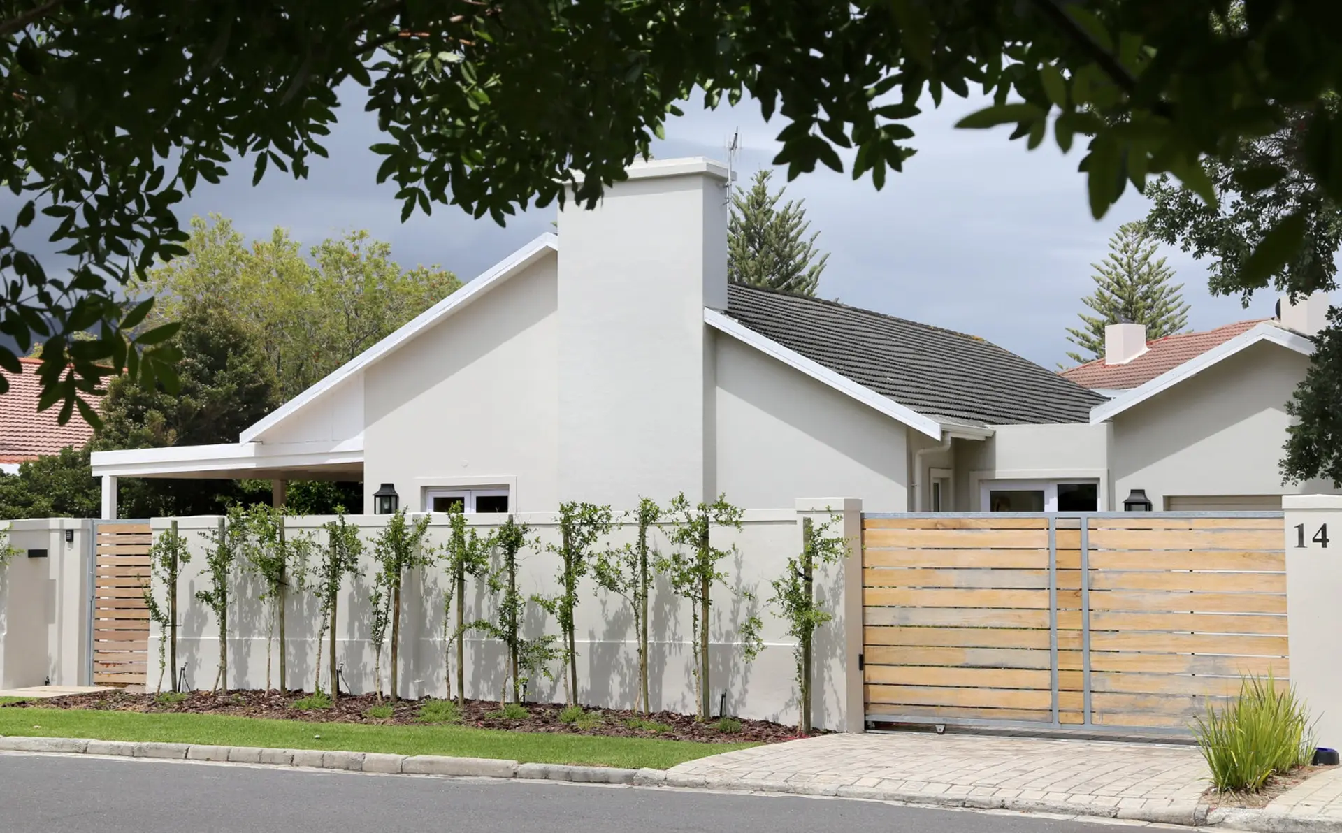 A modern house with a white exterior, a grey tiled roof, and a wooden gate.