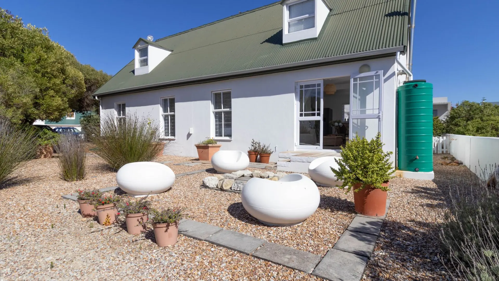 A modern white house with a green roof and a large green water tank outside.