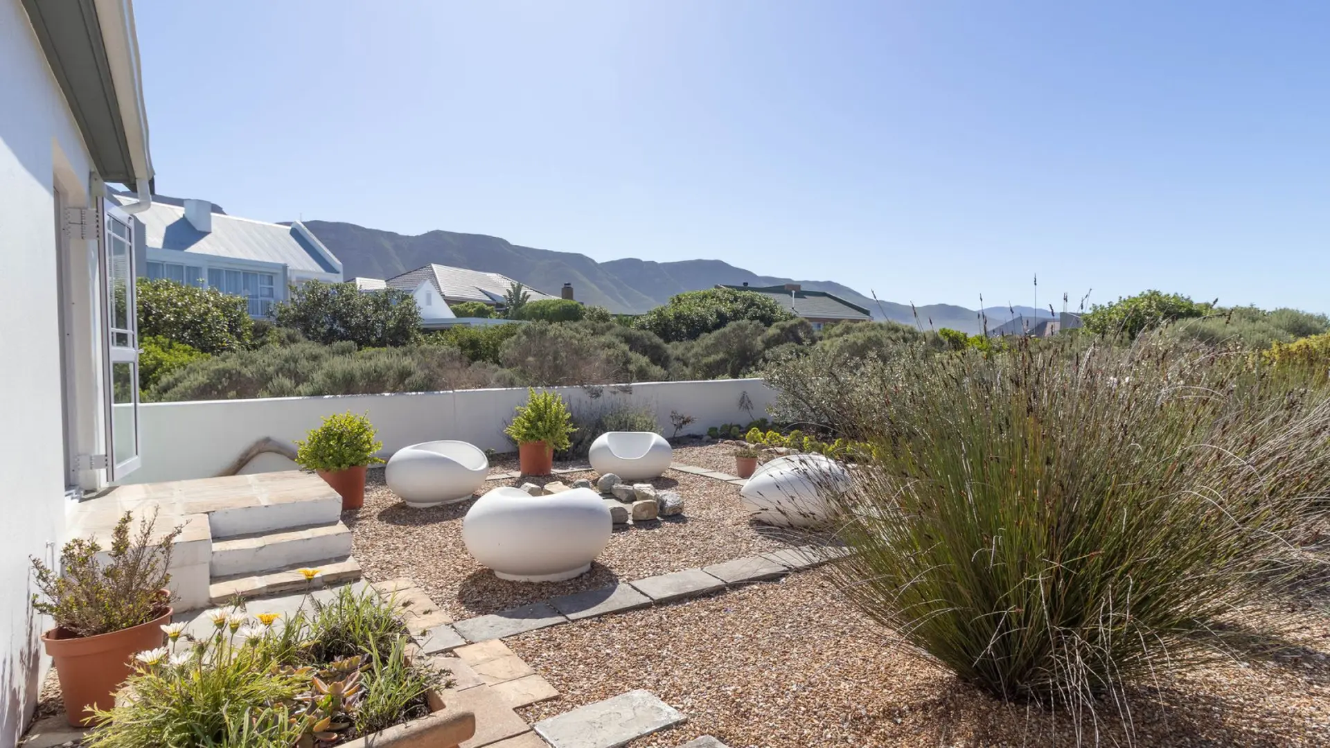 Modern outdoor seating area with white chairs, gravel, plants, and a mountain view.