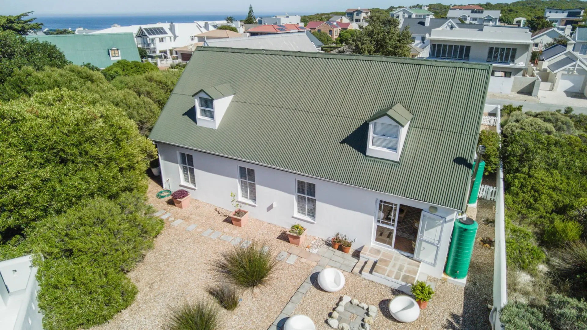 Aerial view of a white house with a green roof and dormer windows in a coastal town.