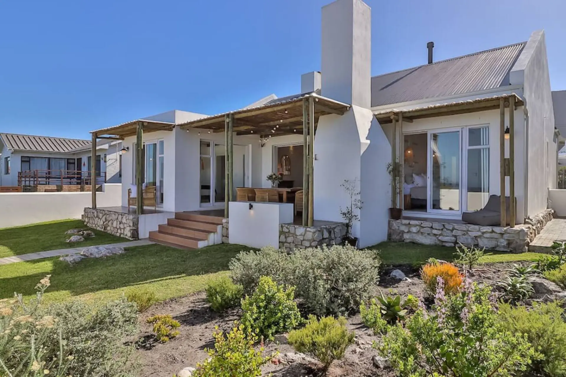 Modern white house with outdoor dining area and scenic garden.
