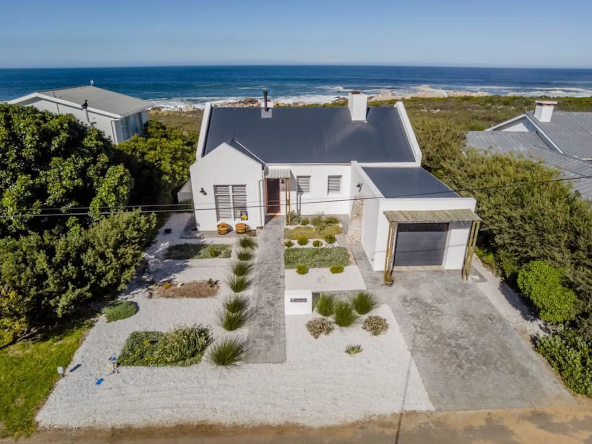 Modern white house with dark roof, near a sandy beach and the ocean.