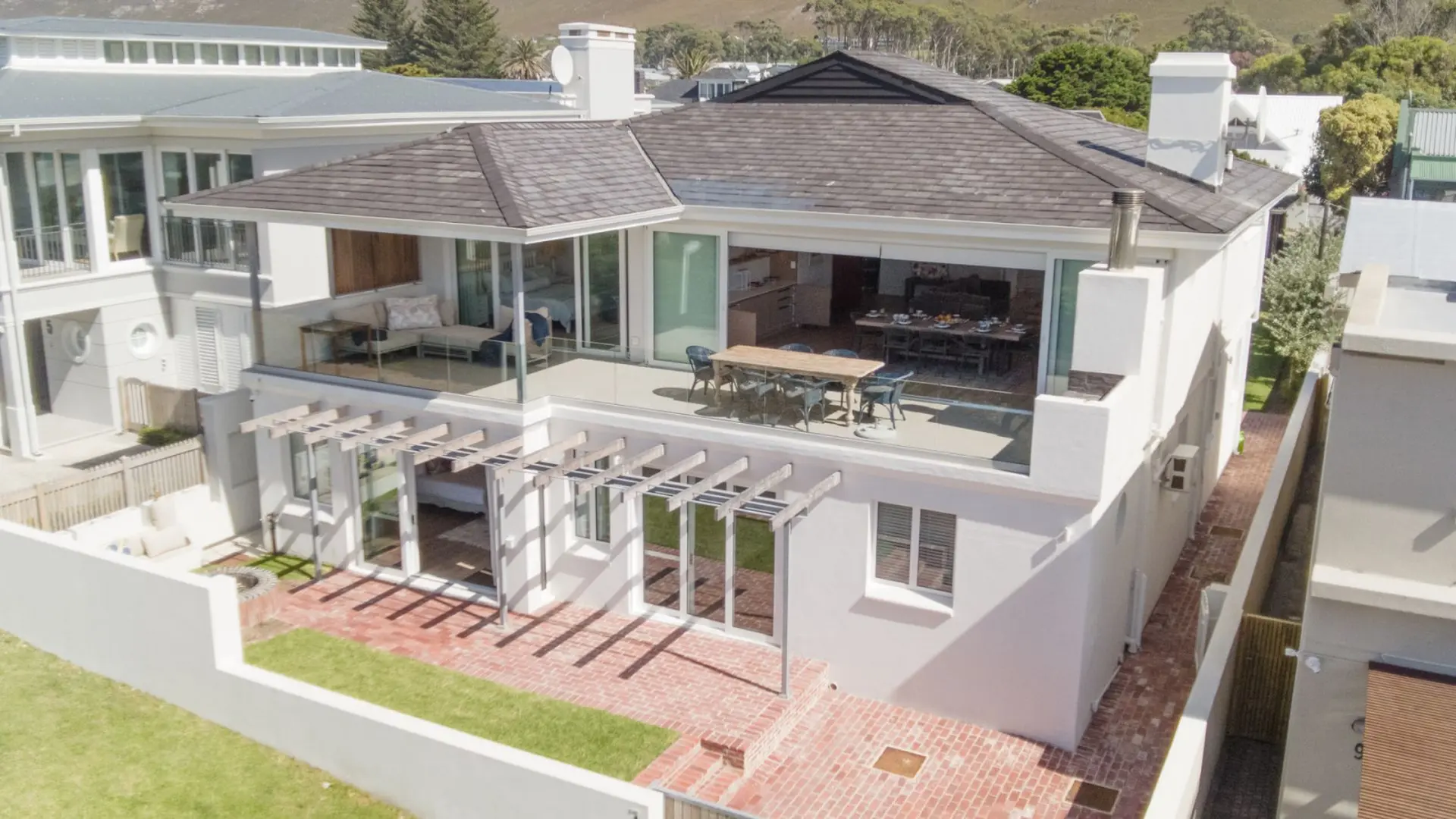 An aerial shot of a modern white house with a dark roof and a large balcony.