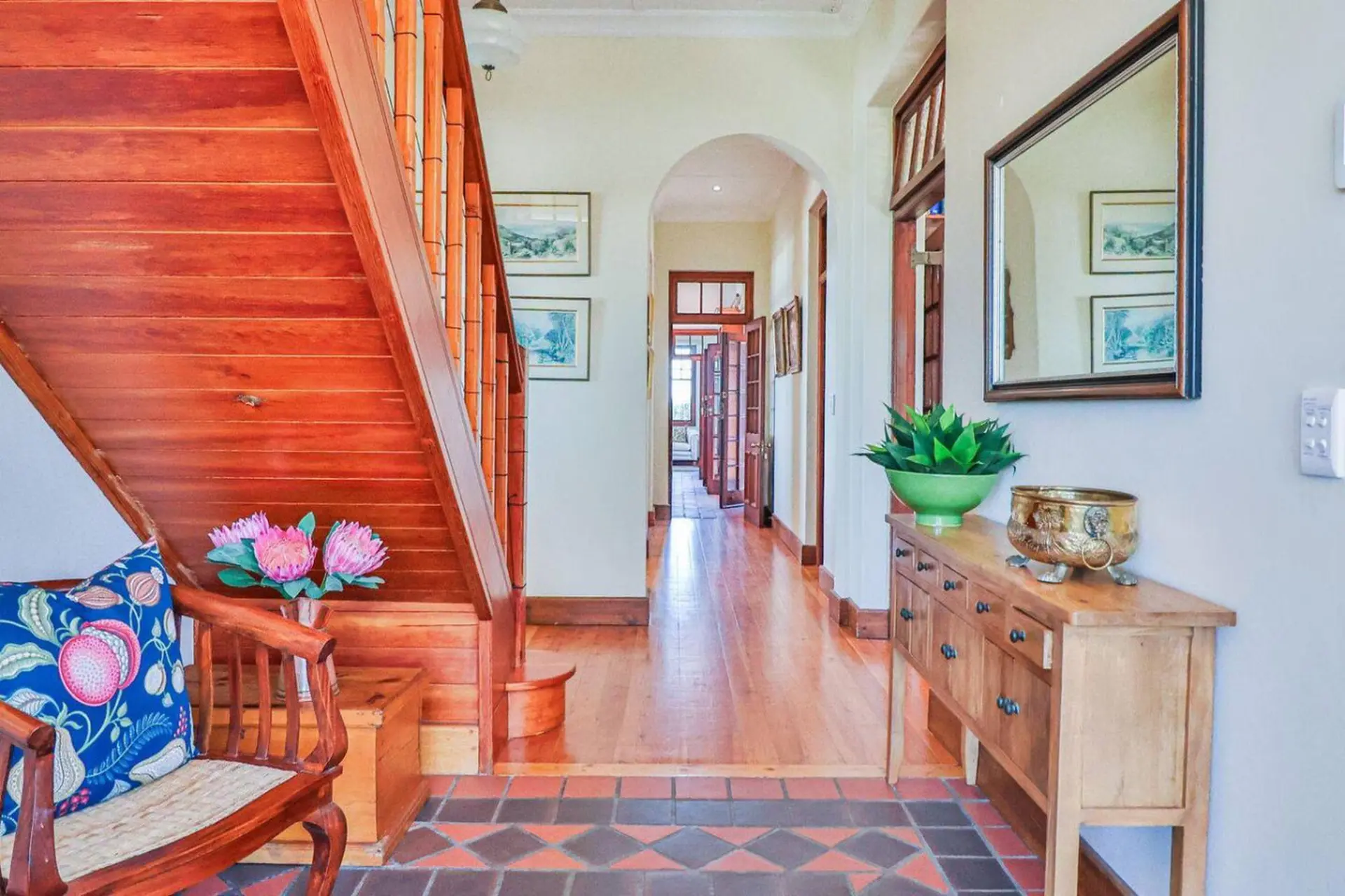A hallway with a wooden staircase, plants, and a mirror.