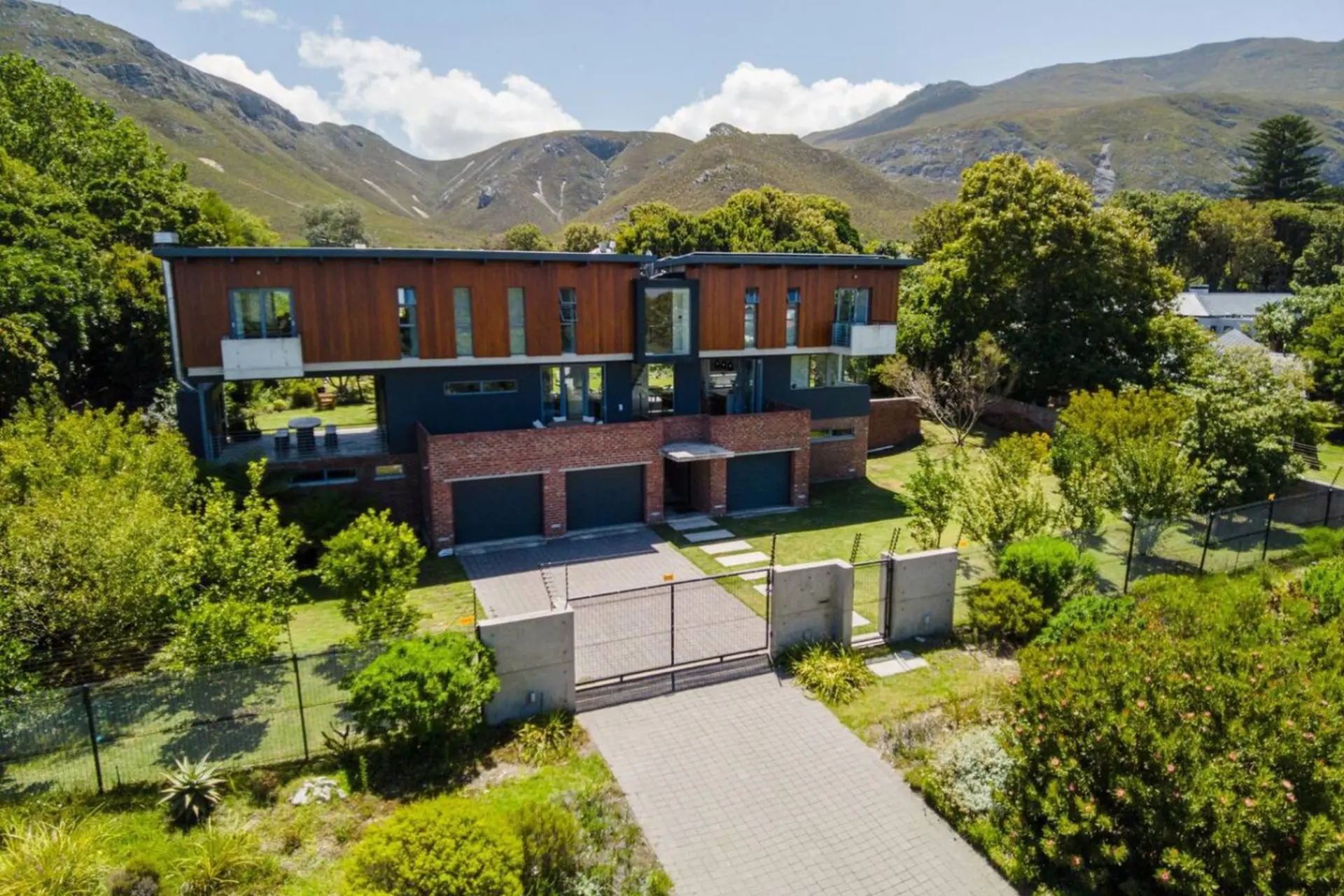 A modern house with wood and brick accents, a three-car garage, and a gated driveway, set against a 