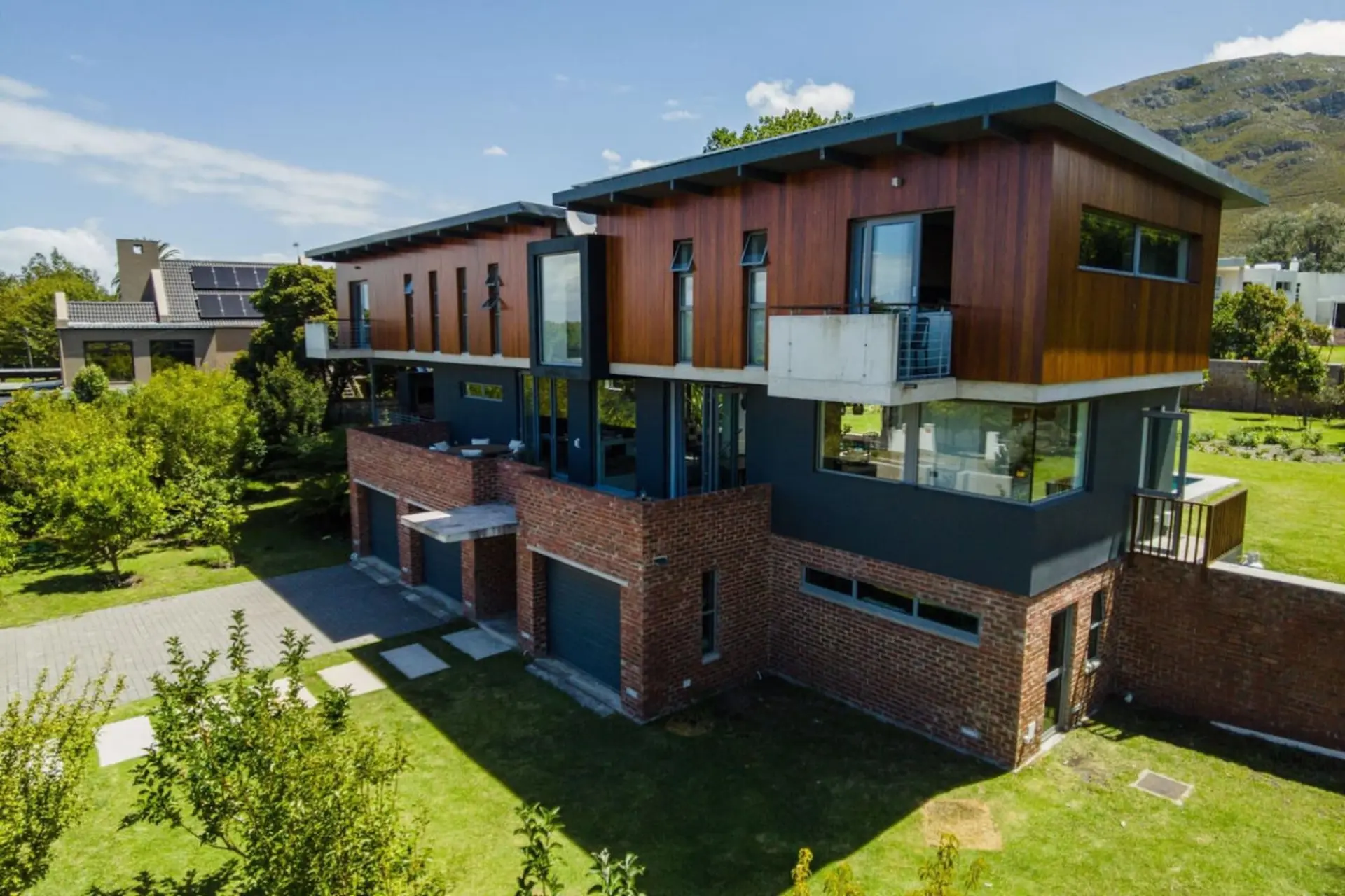 Modern house with wood and brick exterior, large windows, and a green lawn.