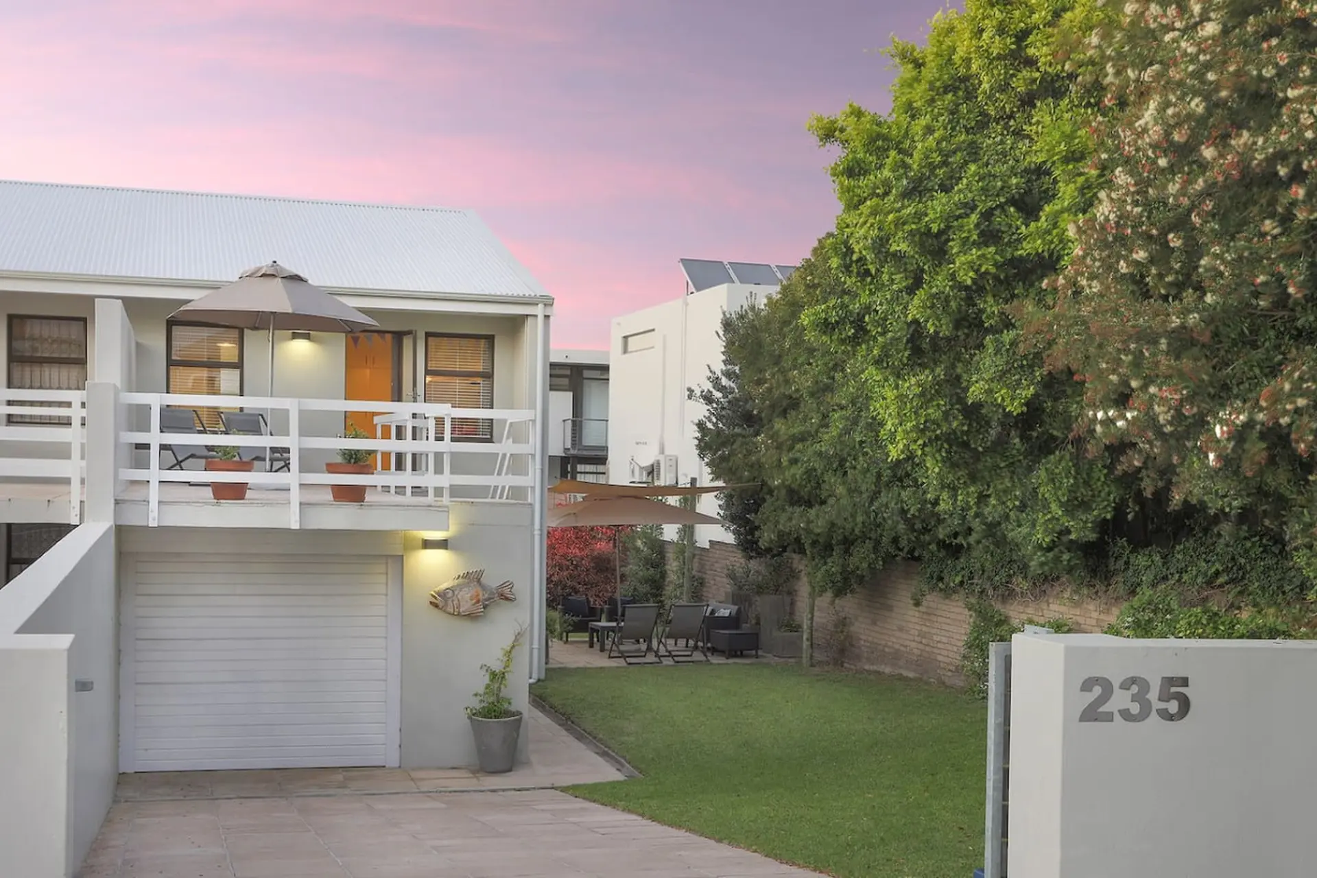 Modern house with white balcony, garage, and garden at sunset.