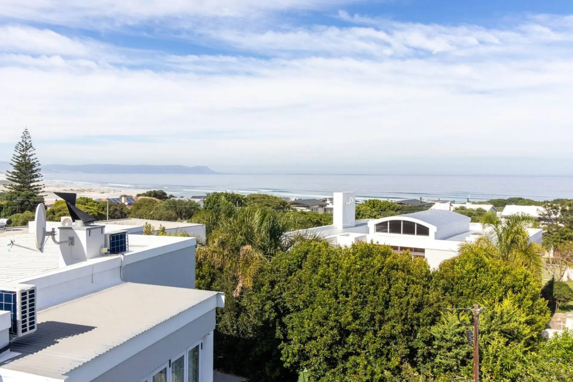 Ocean view from rooftop with modern houses and lush greenery.