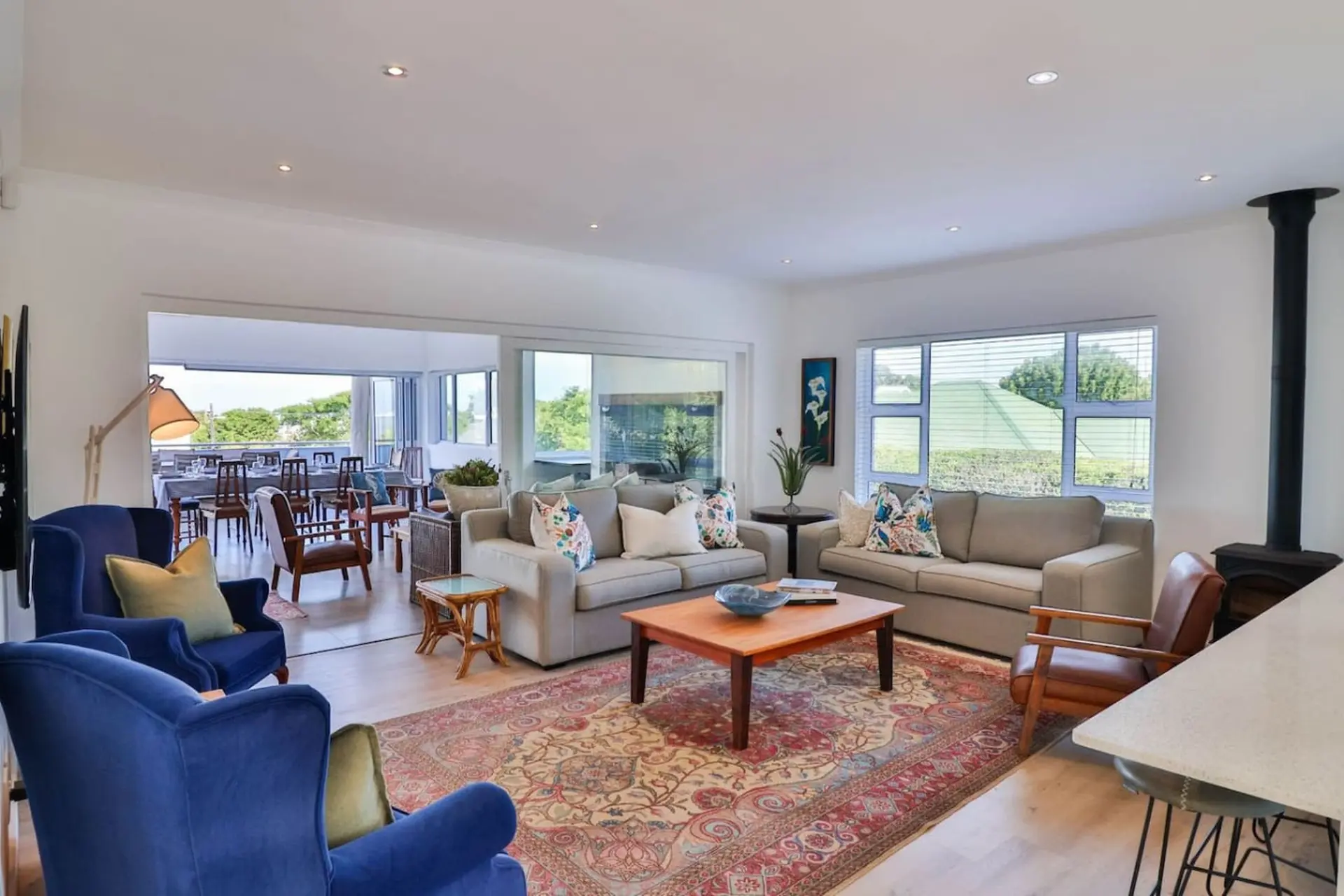 Living room with plush blue armchairs, neutral sofas, and a vintage rug.
