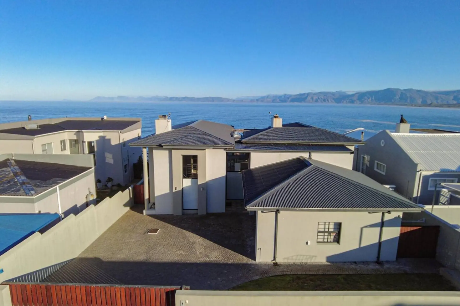 Modern house with a grey roof and large windows, facing the ocean.