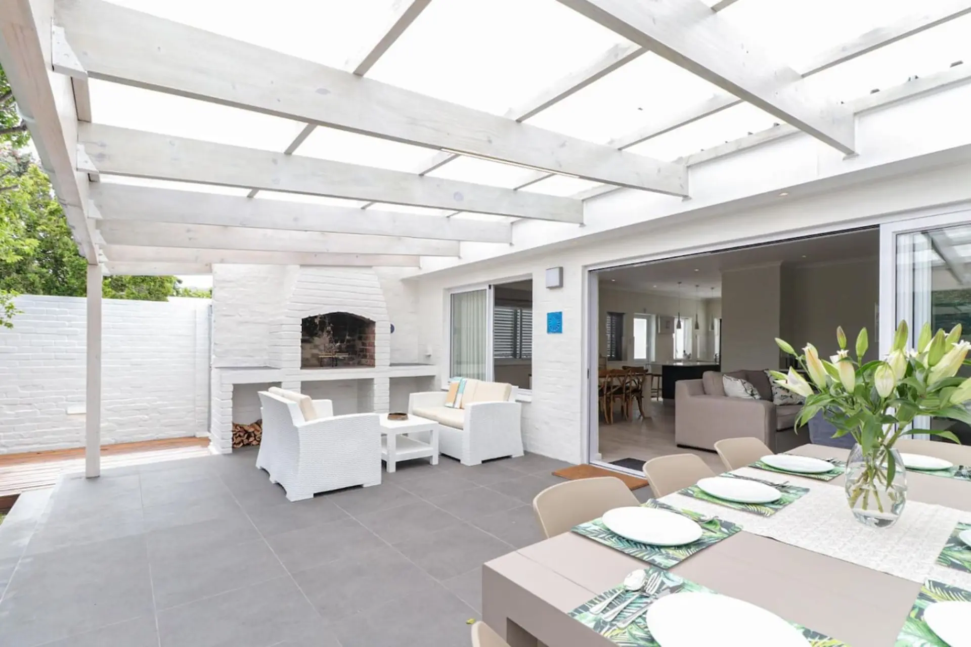 An outdoor dining area with a patio, fireplace, and seating, opening into a living room.