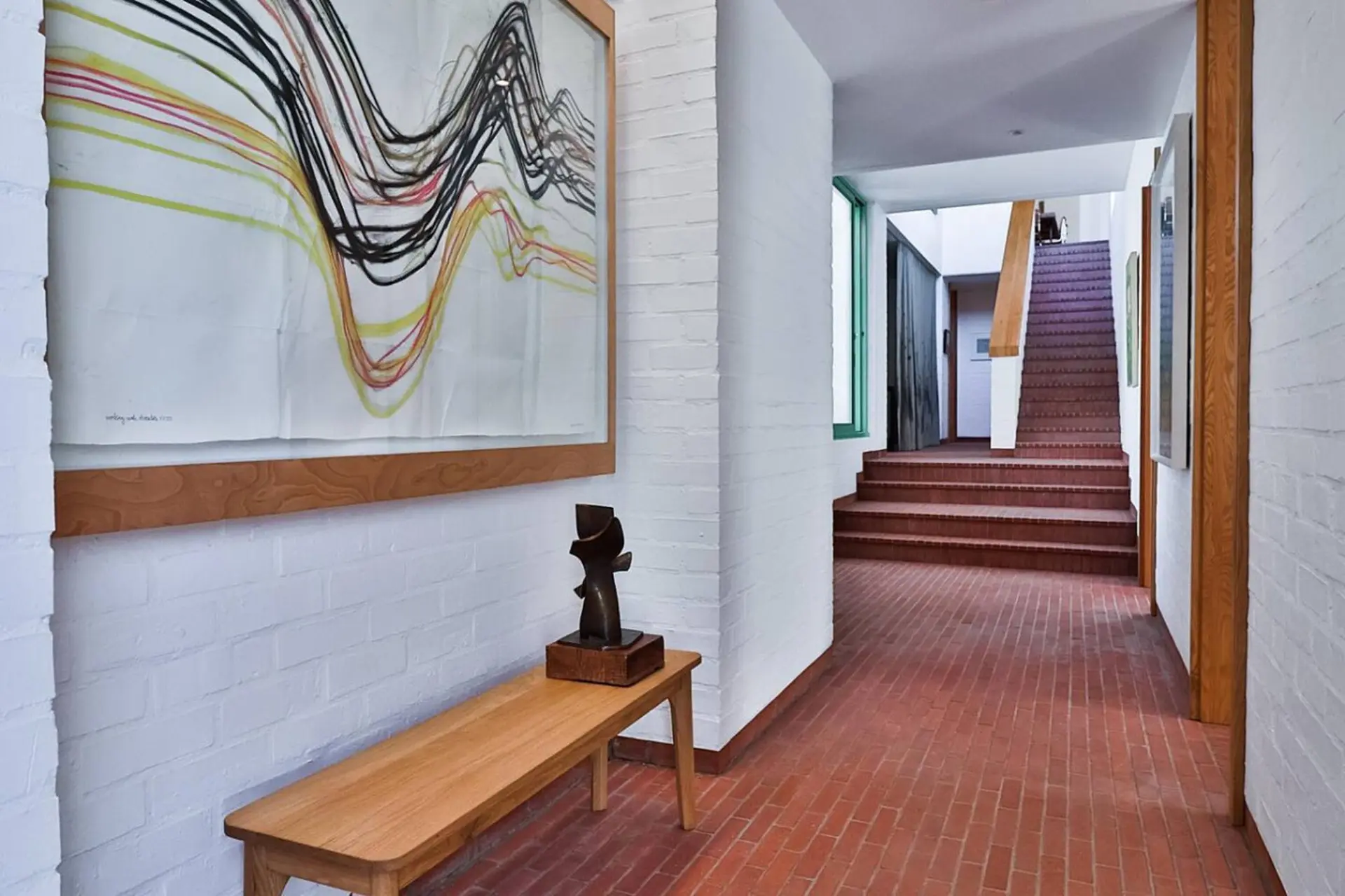 Hallway with brick floor, white brick walls, a bench, and stairs.