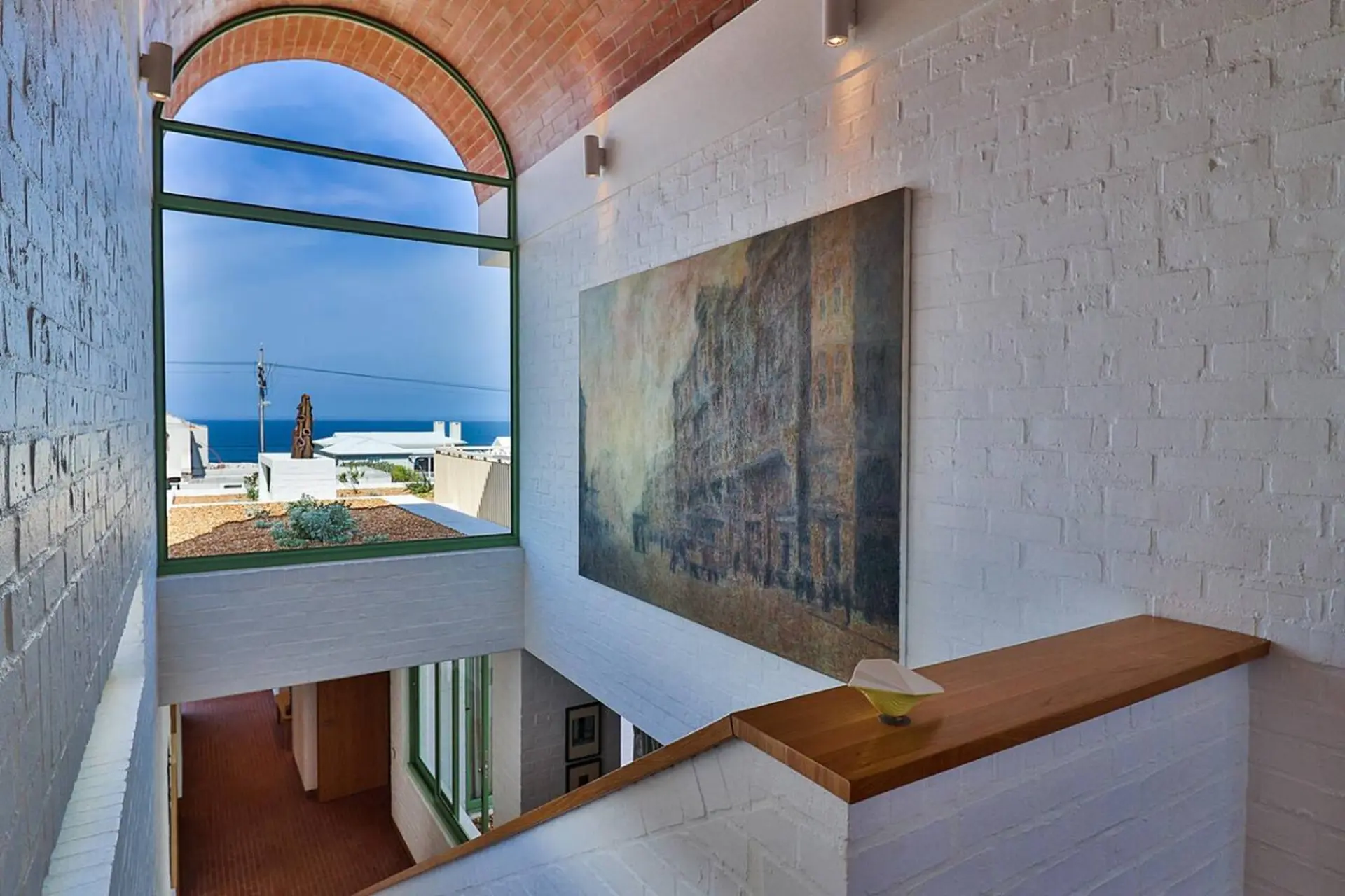 A modern staircase with white brick walls, a large painting, and a view of the ocean.