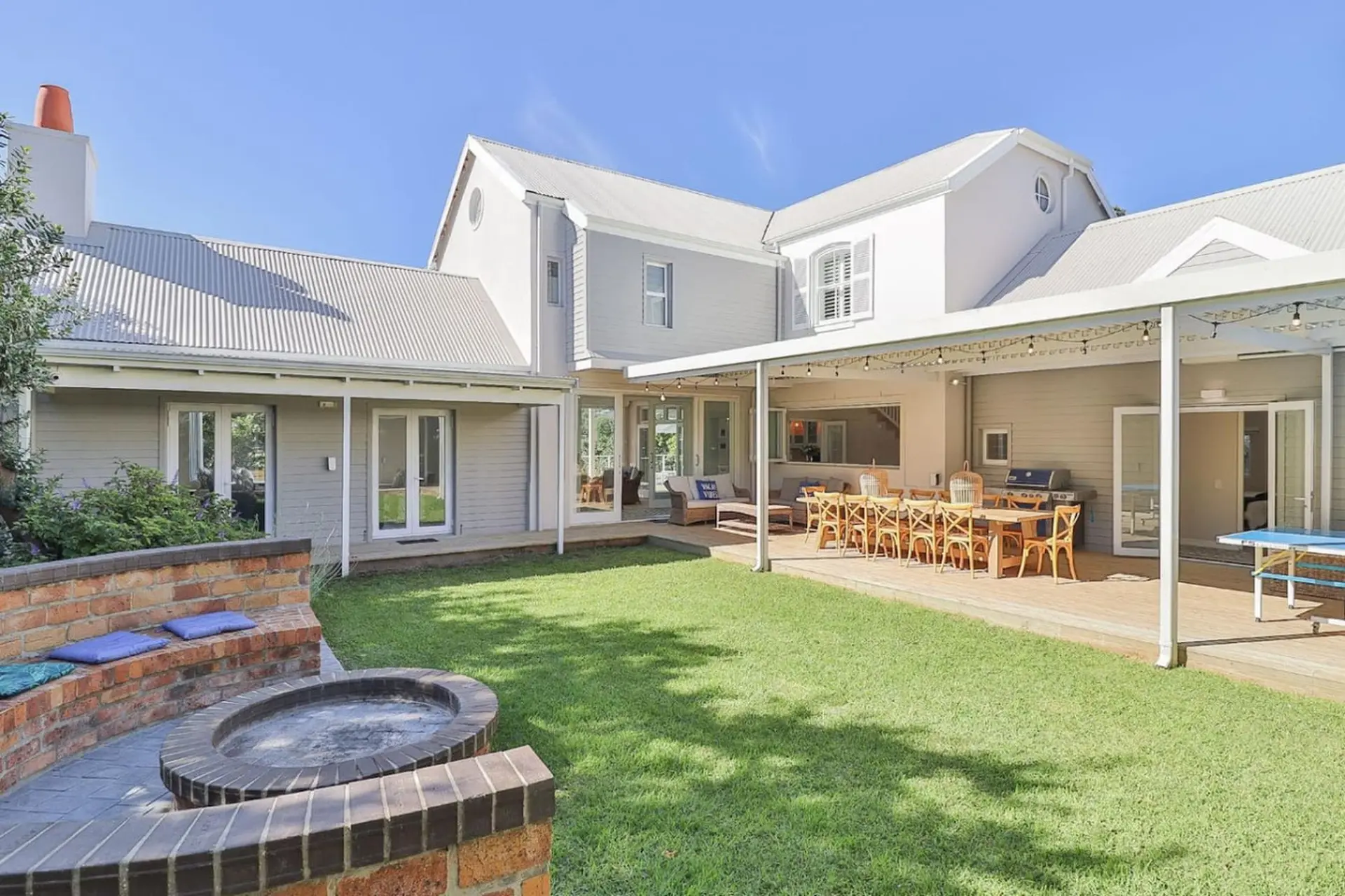 A large grey house with a white roof, outdoor dining area, and fire pit.