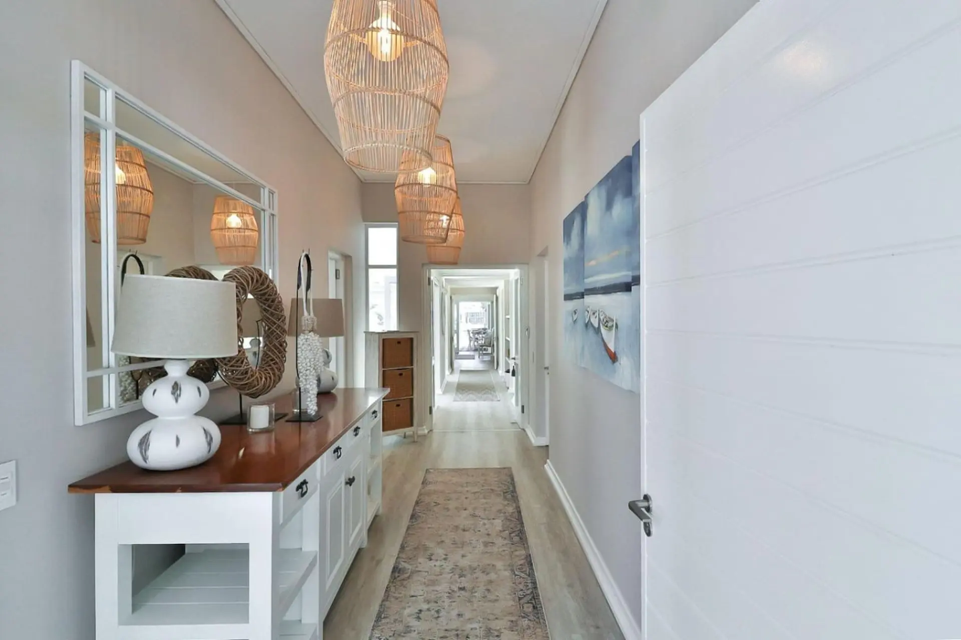 Hallway with white sideboard, artwork, rattan pendant lights and a doorway.