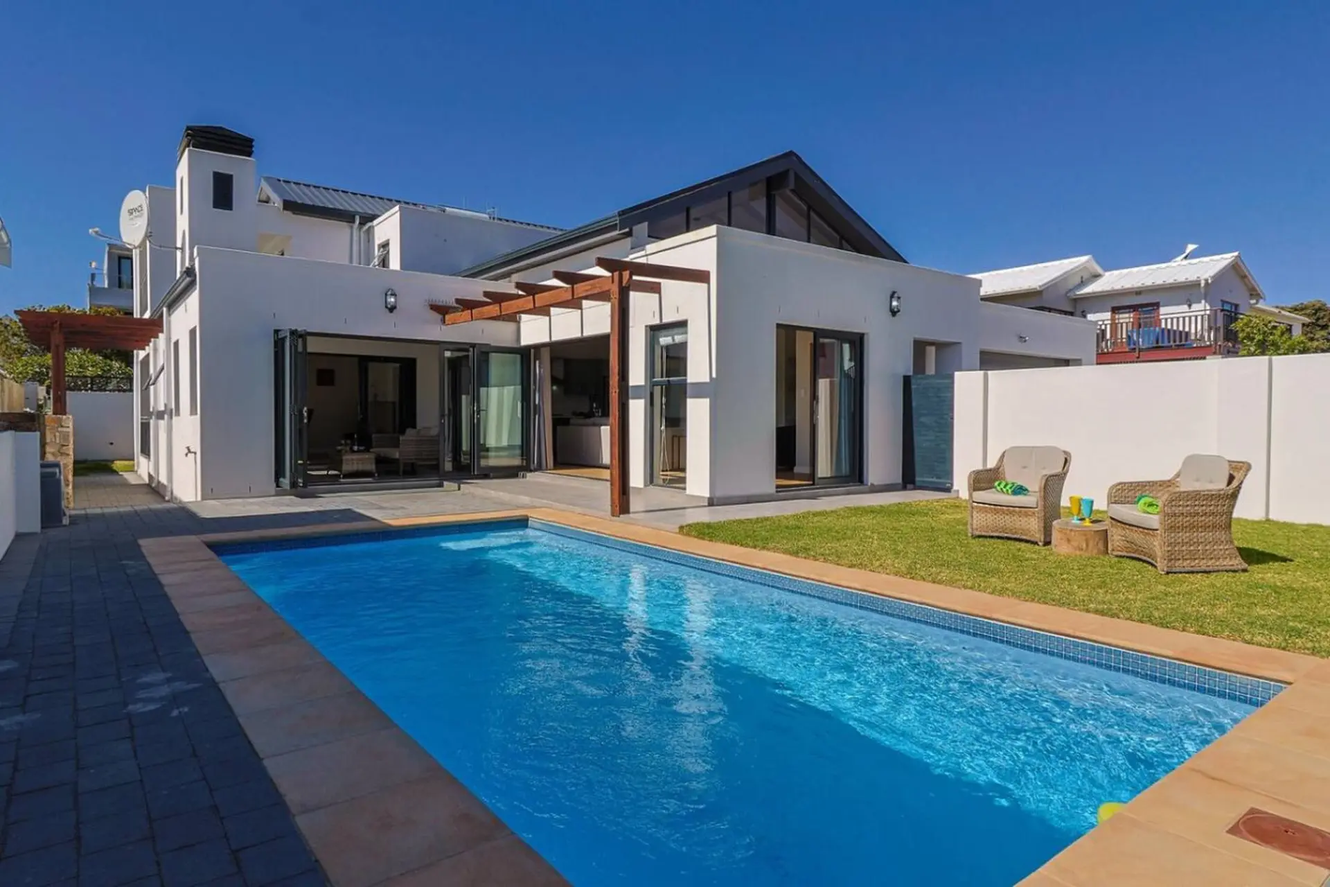 A modern white house with a swimming pool and two chairs on the lawn.