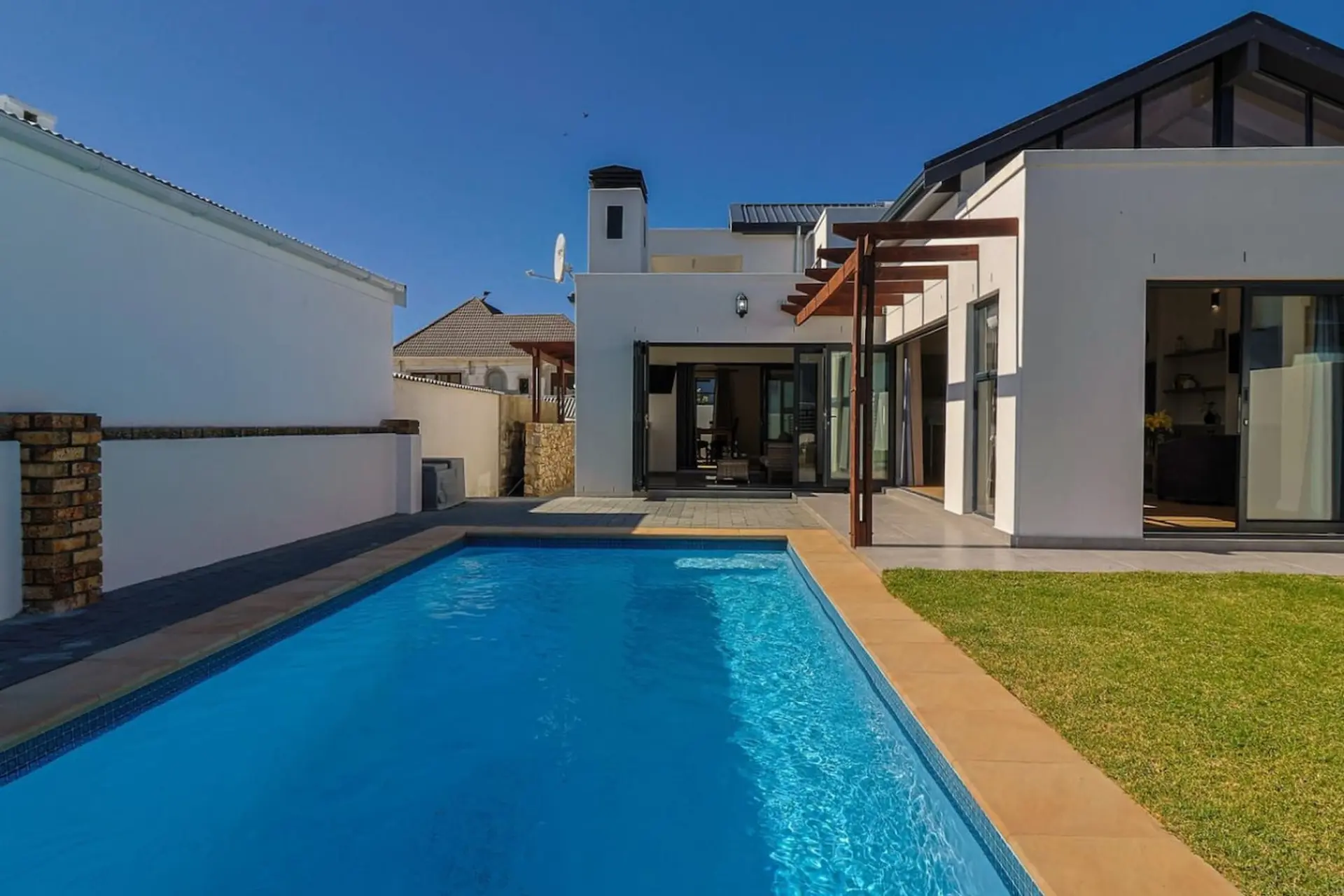 A modern white house with a swimming pool and green lawn.