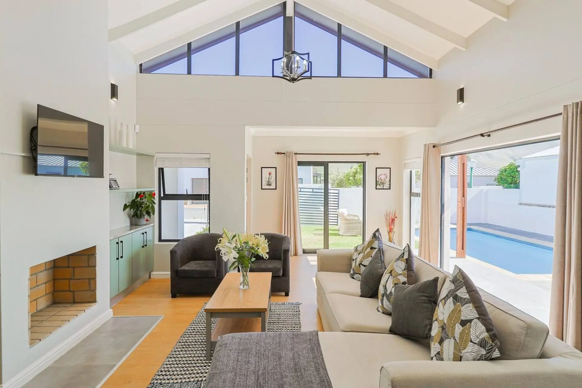 Modern living room with a vaulted ceiling, fireplace, and view of a swimming pool.