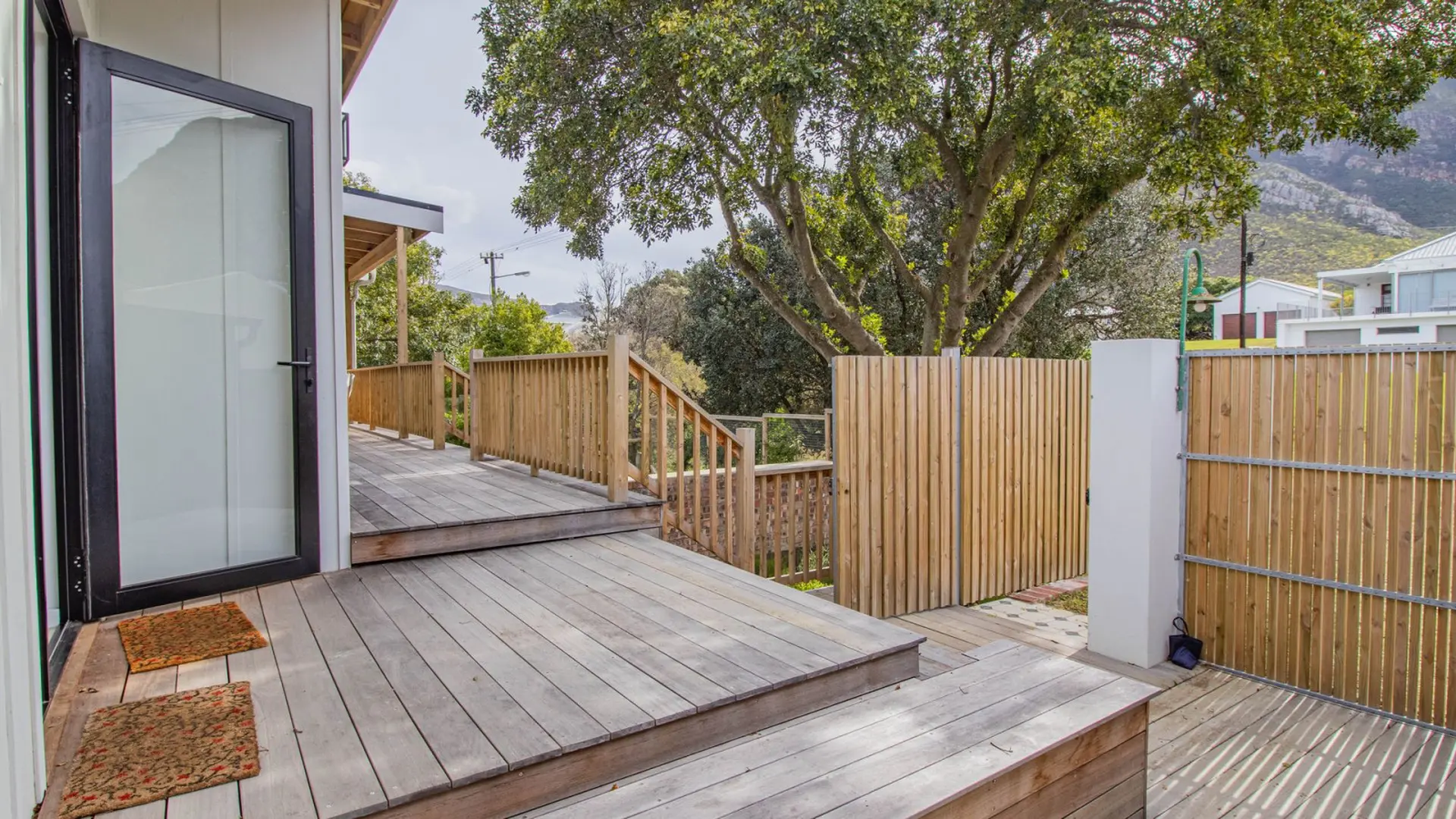 Wooden deck and fence with a glass door, leading to stairs under a tree.