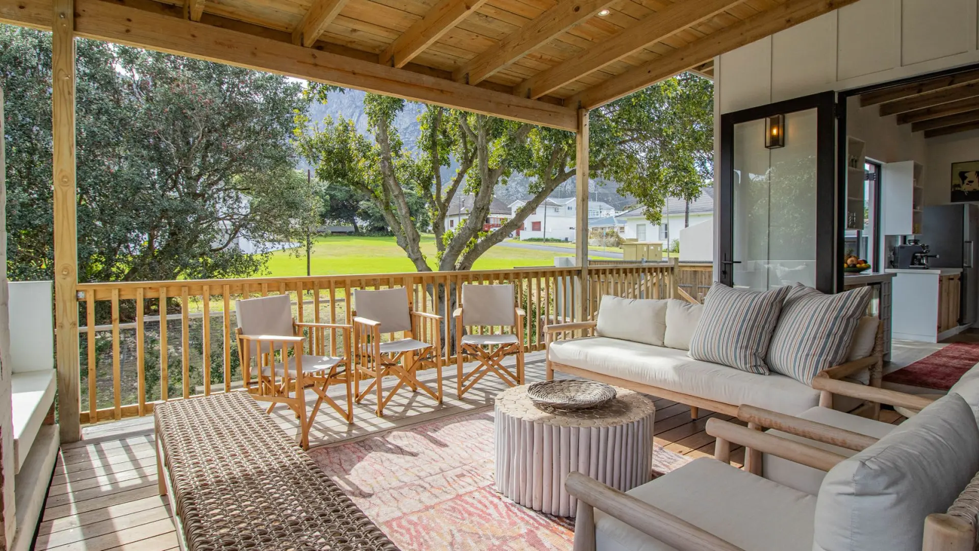 Deck with wooden furniture and view of a green field and trees.