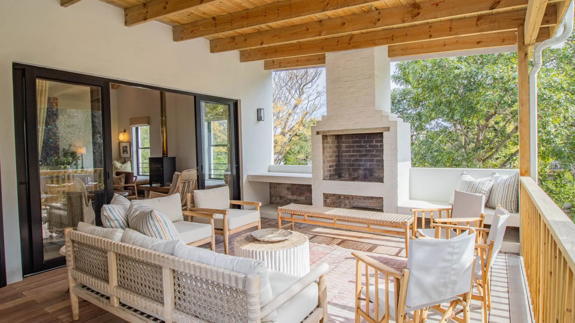 Cozy patio with a fireplace, sofas, and chairs, overlooking trees.