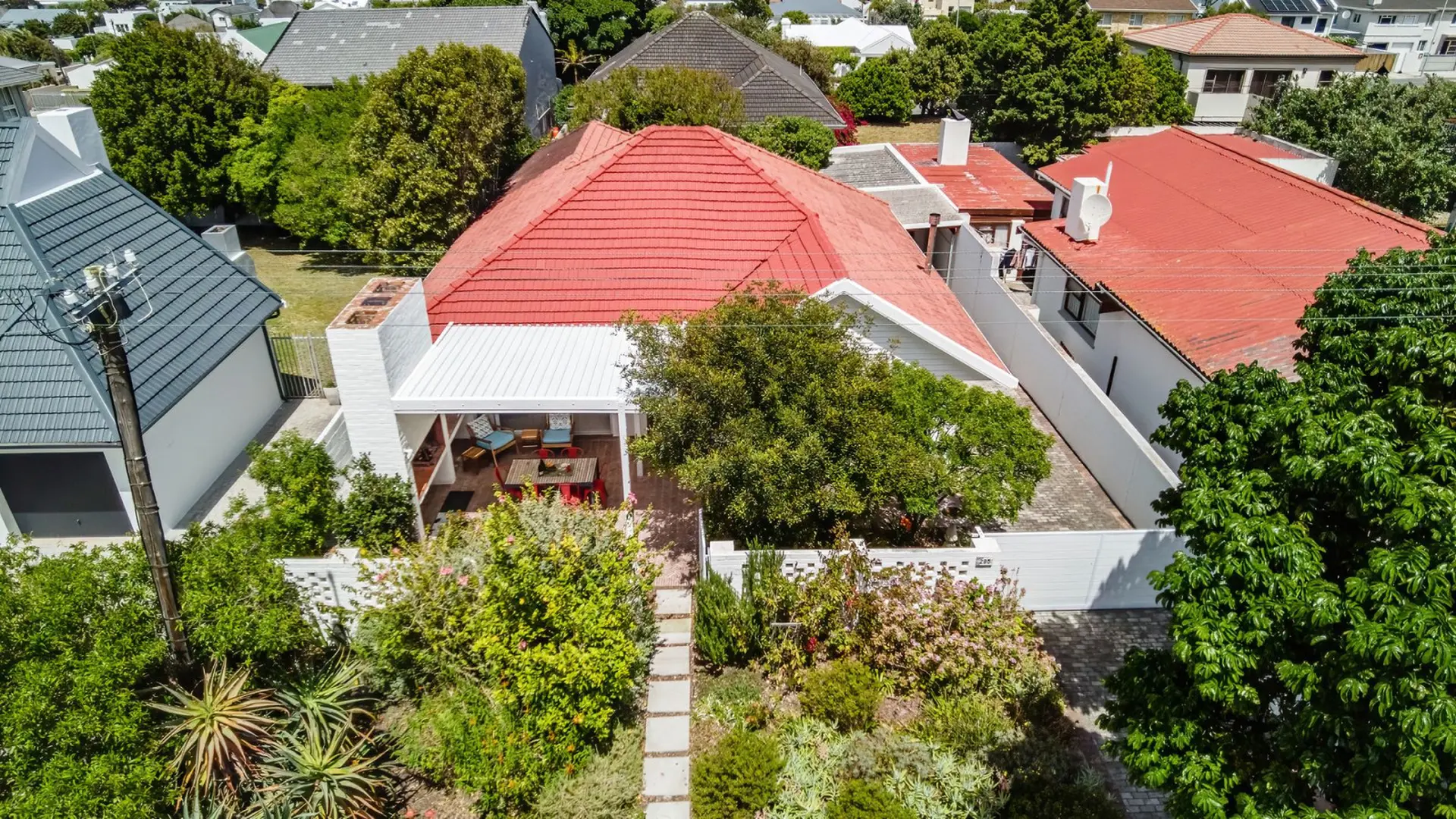 Aerial view of a white house with a red tile roof, surrounded by lush green trees and gardens.