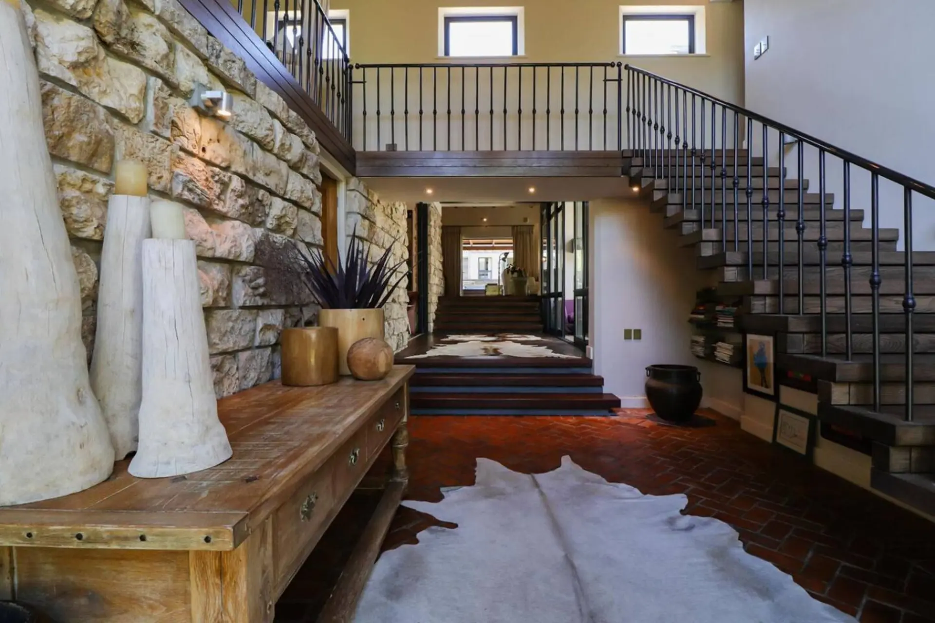 Grand entryway with stone walls, a wooden console table, cowhide rugs, and a rustic staircase.