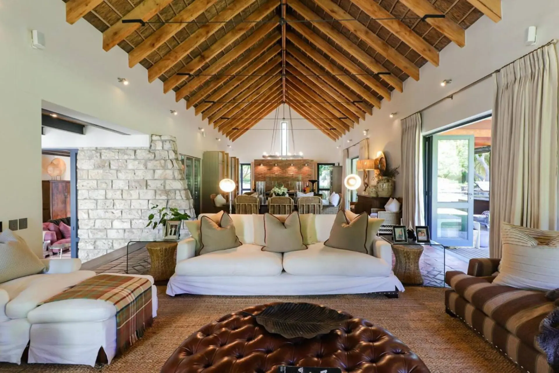 A luxurious living room with a thatched roof, stone fireplace, and comfortable seating.