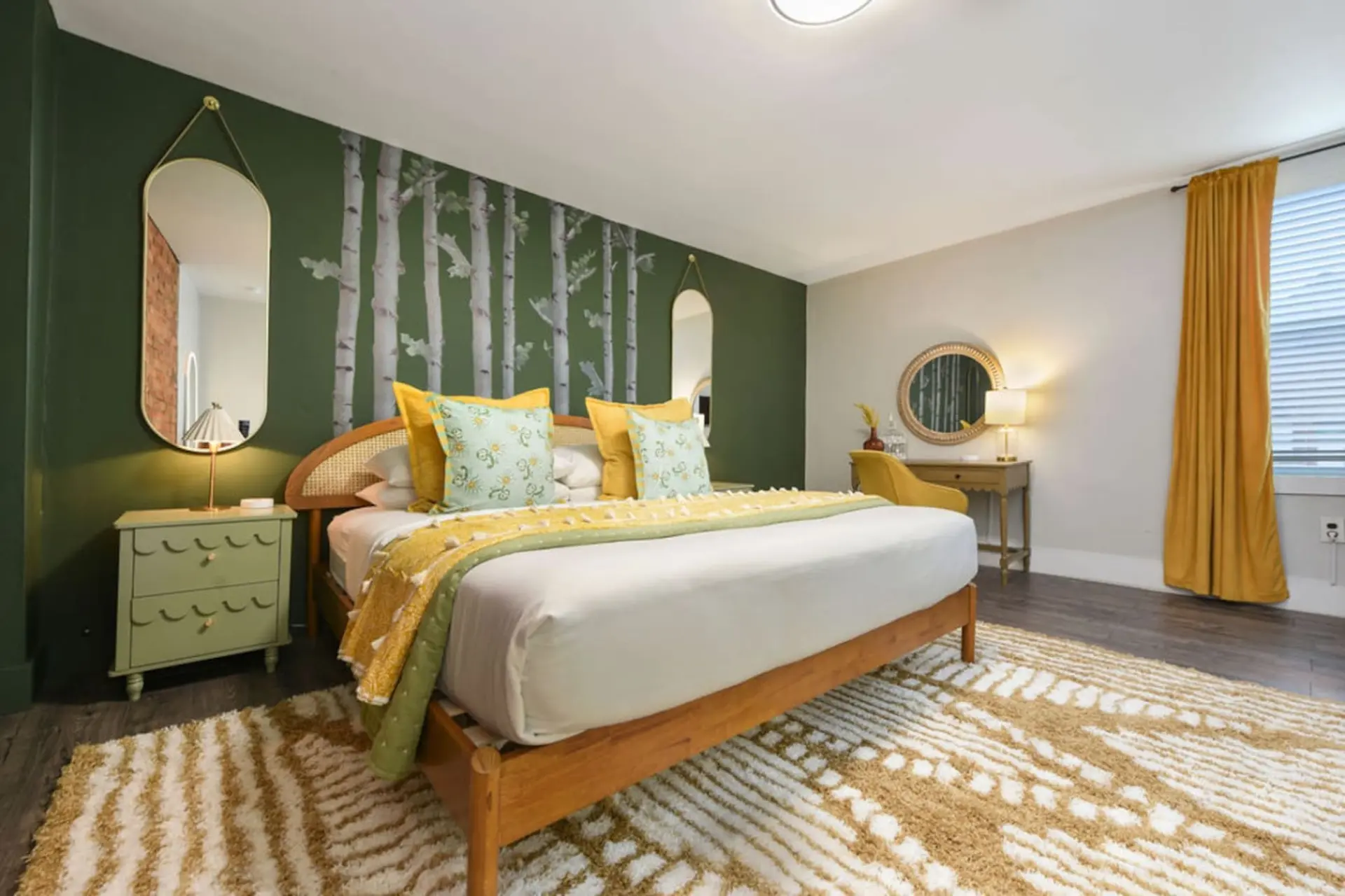 Bedroom with green walls, a birch tree mural, a wooden bed, and yellow accents.