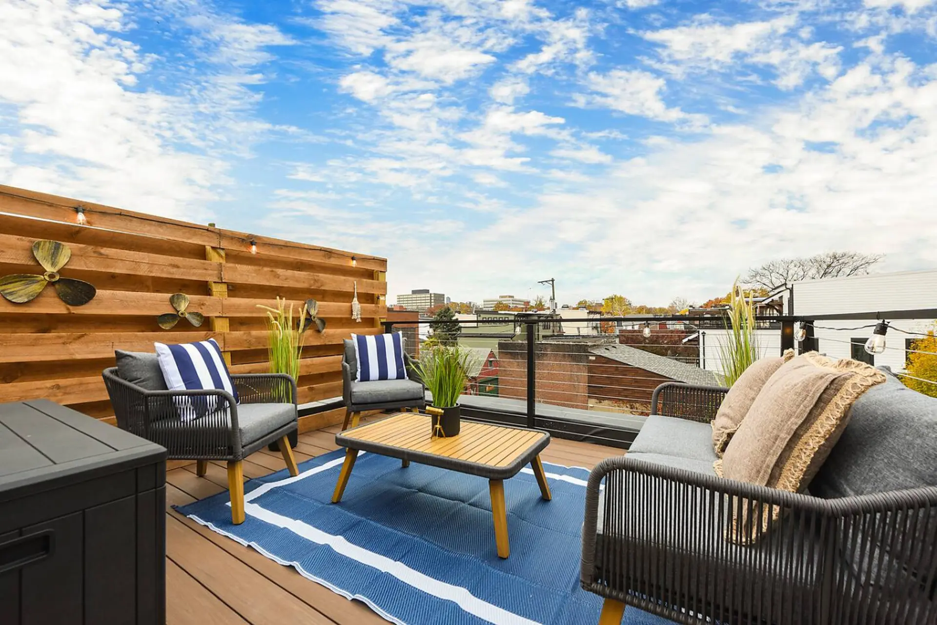 Rooftop patio with seating, coffee table, and city views under a cloudy sky.