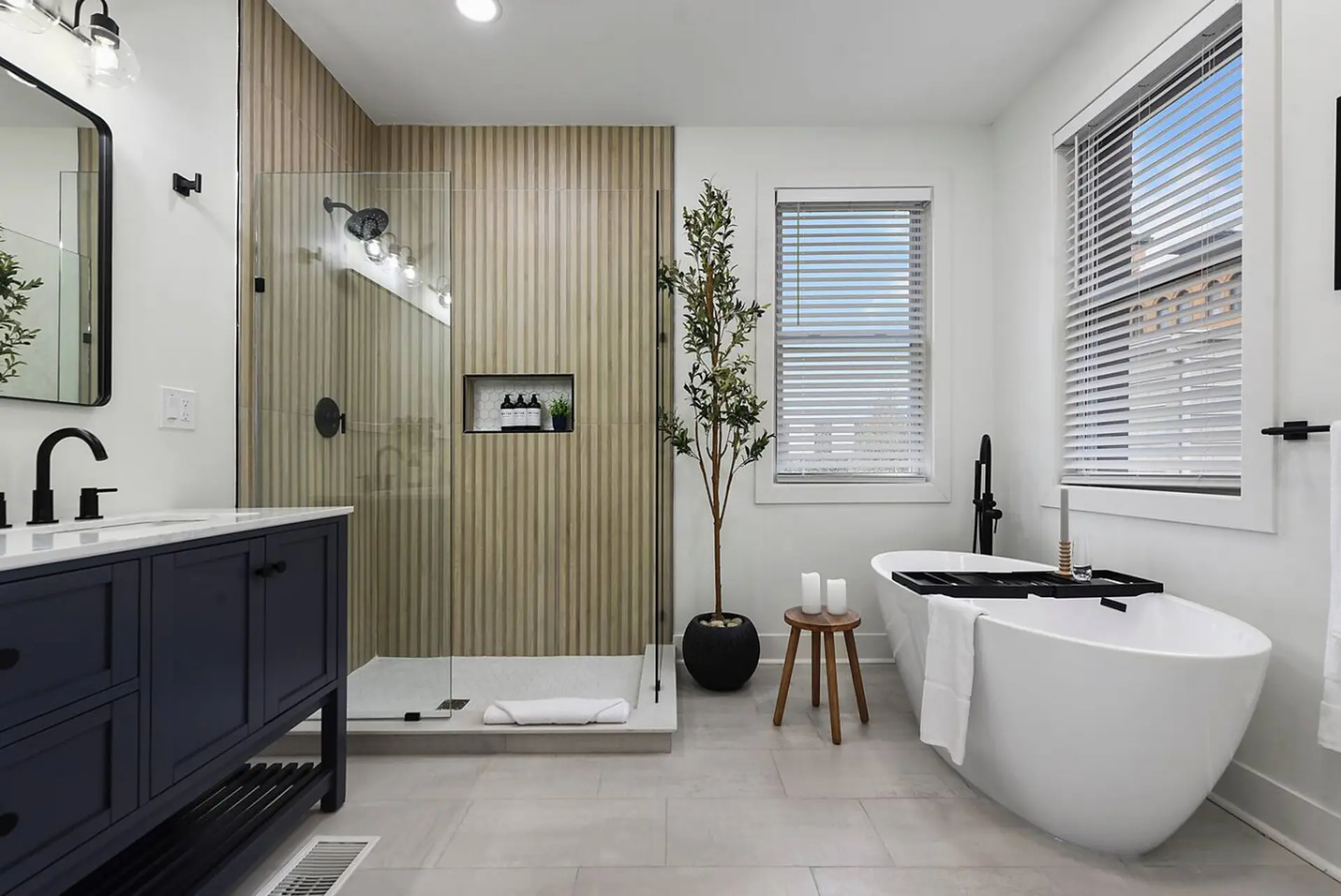 A modern bathroom with a dark blue vanity, freestanding tub, and a walk-in shower.