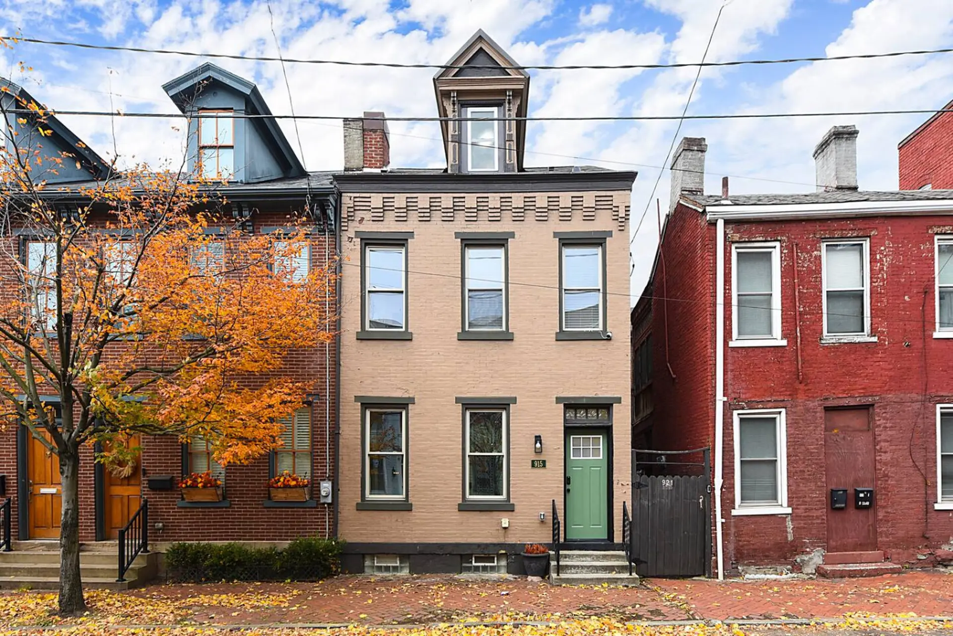 Autumn scene of a row of brick townhouses, one painted tan with a green door.