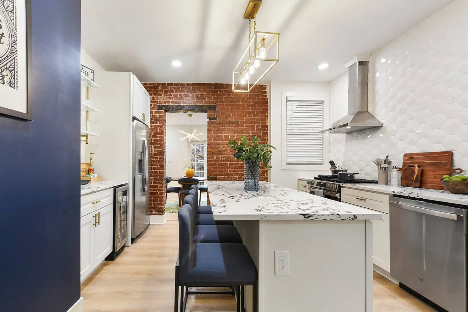 A modern kitchen with white cabinets, stainless steel appliances, and a brick accent wall.