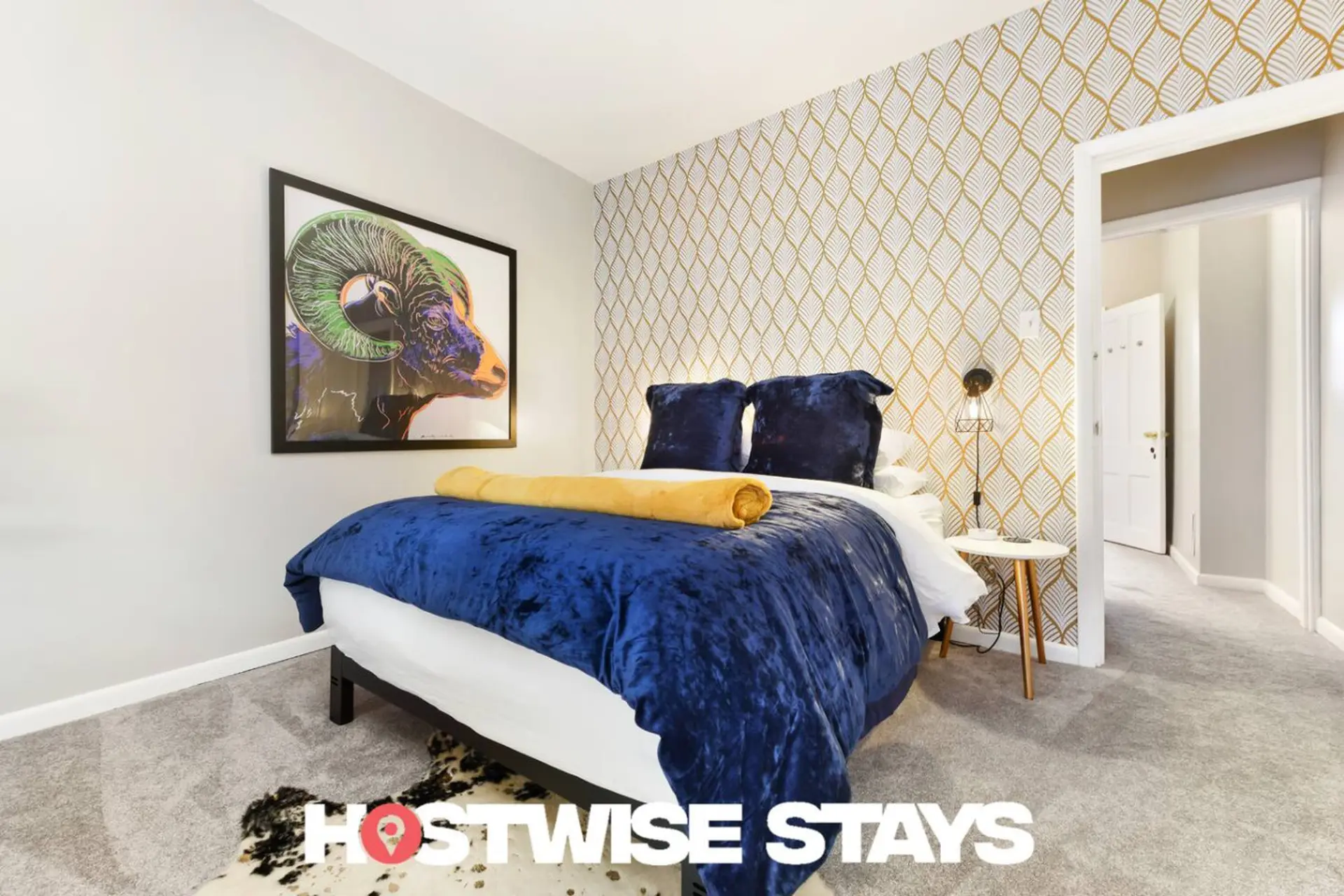 A bedroom with a royal blue velvet comforter, a yellow throw blanket, and artwork of a ram.