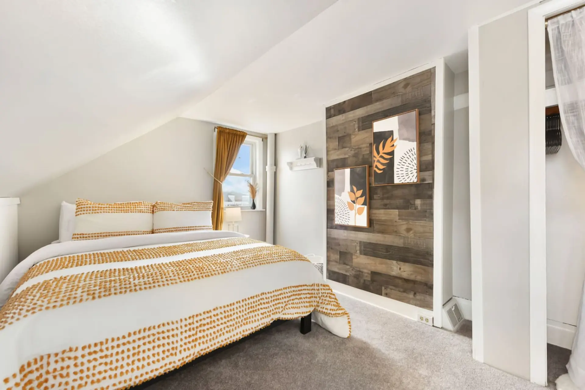 Cozy attic bedroom with a queen bed, rustic wood accent wall, and modern art.