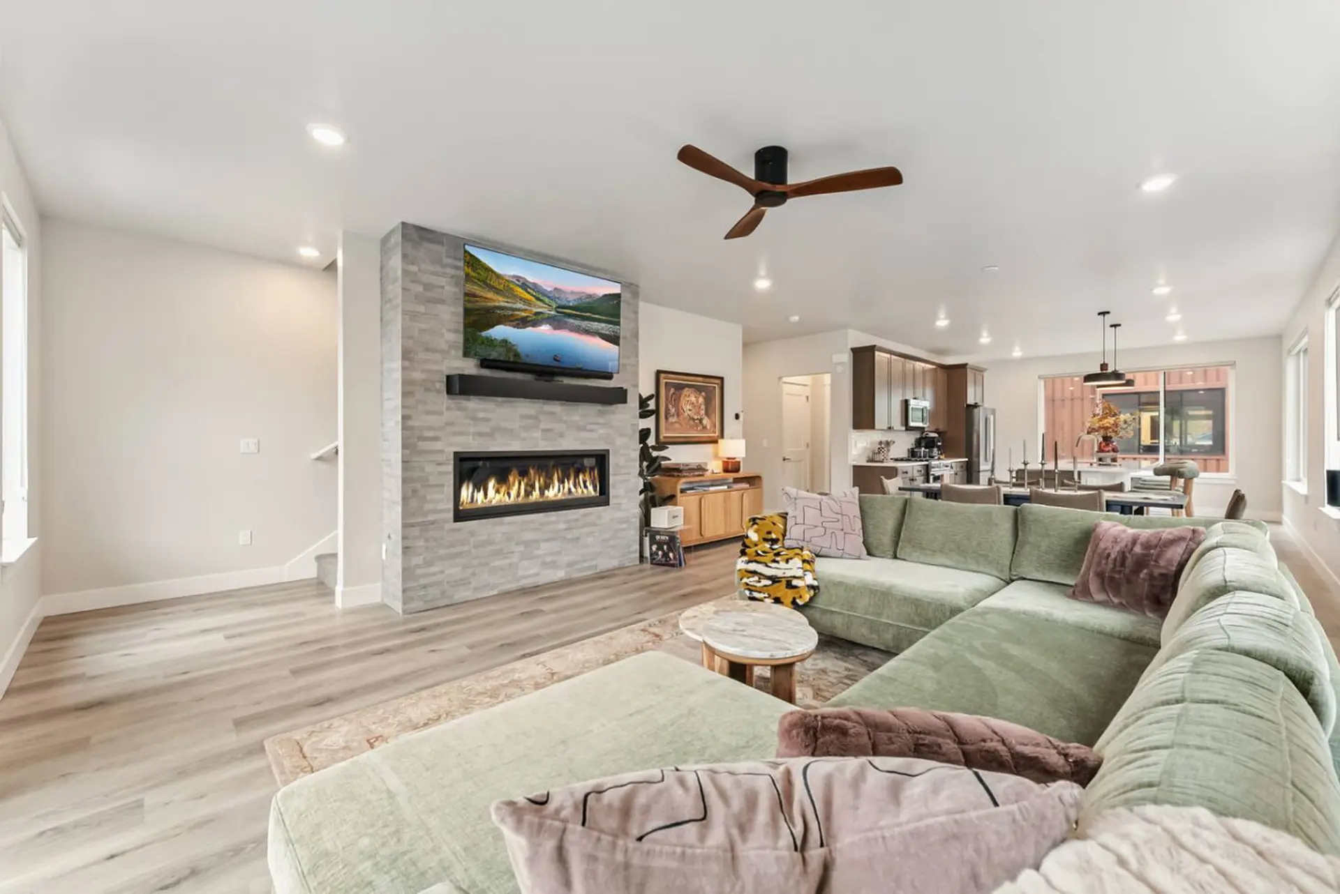 A modern living room with a green sectional sofa, fireplace, and TV.
