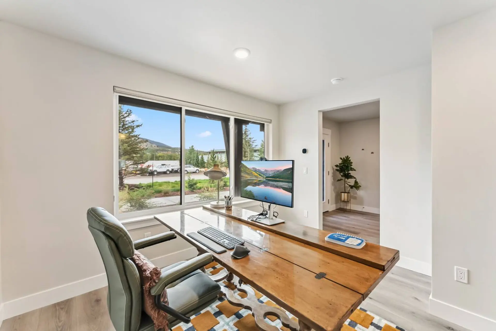 A desk with a monitor, keyboard, and mouse faces a window.