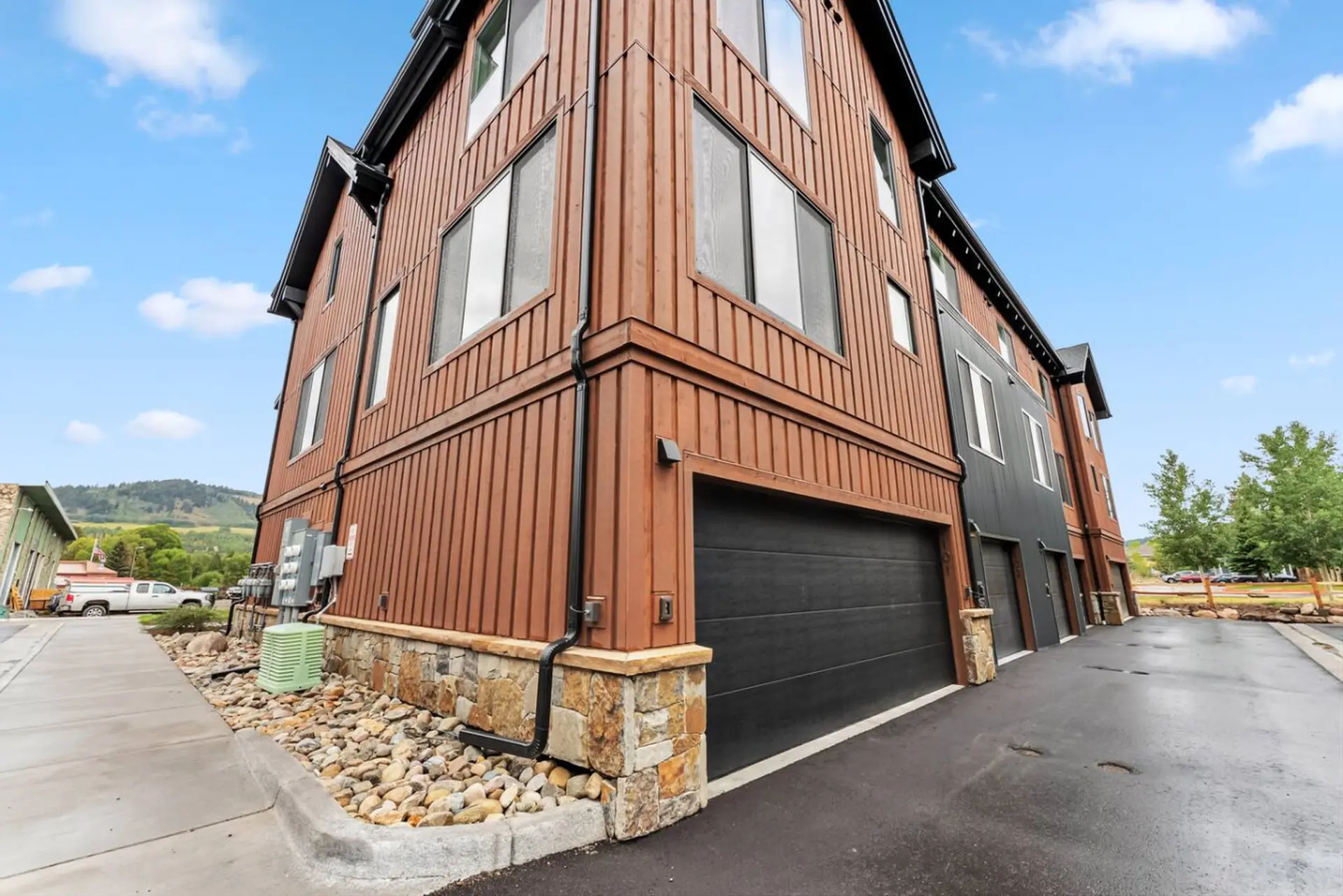 Modern townhouse with brown wood siding, stone foundation, and black garage doors.
