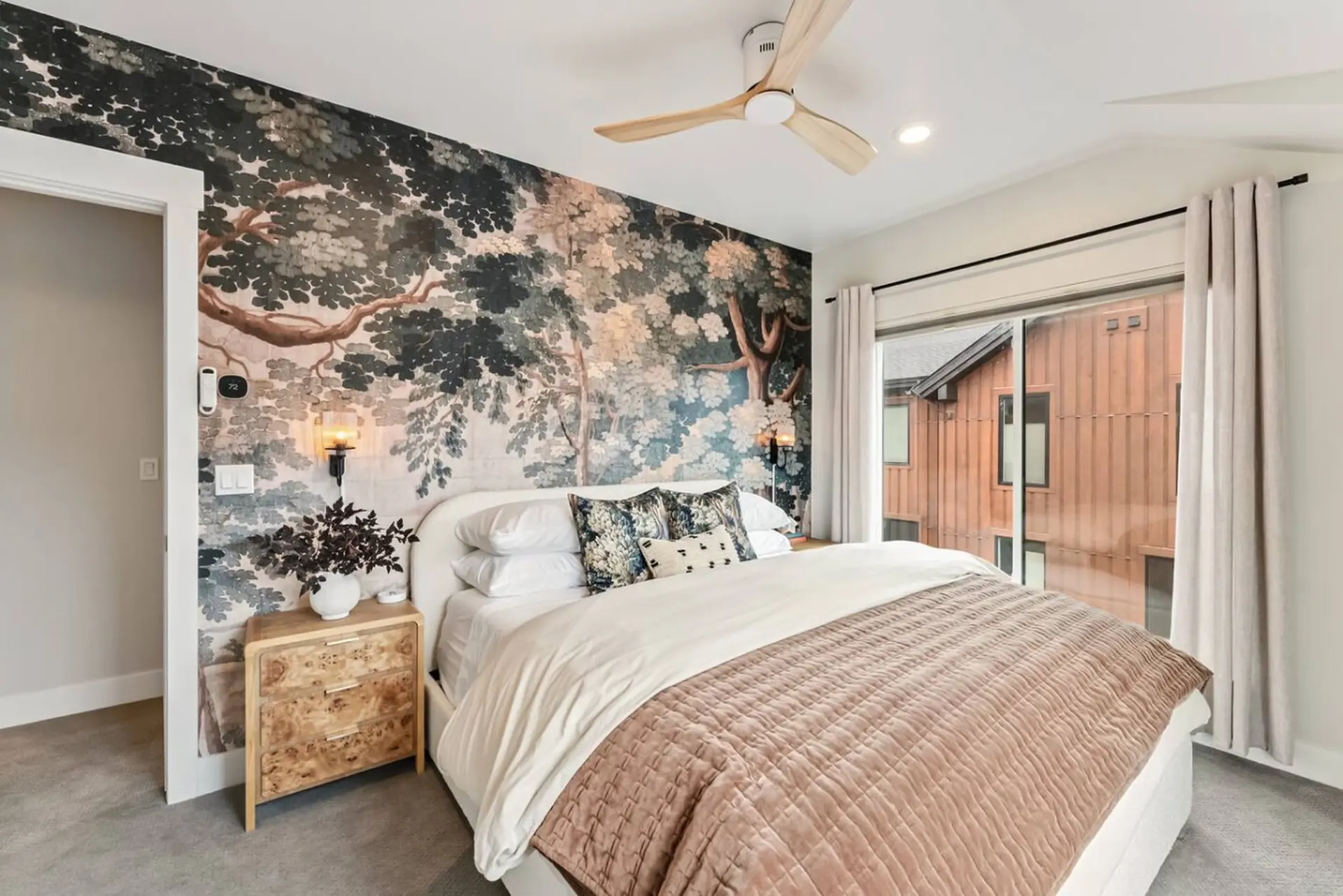 A bedroom with a mural wallpaper, a bed with white bedding, and a textured rust-colored quilt.