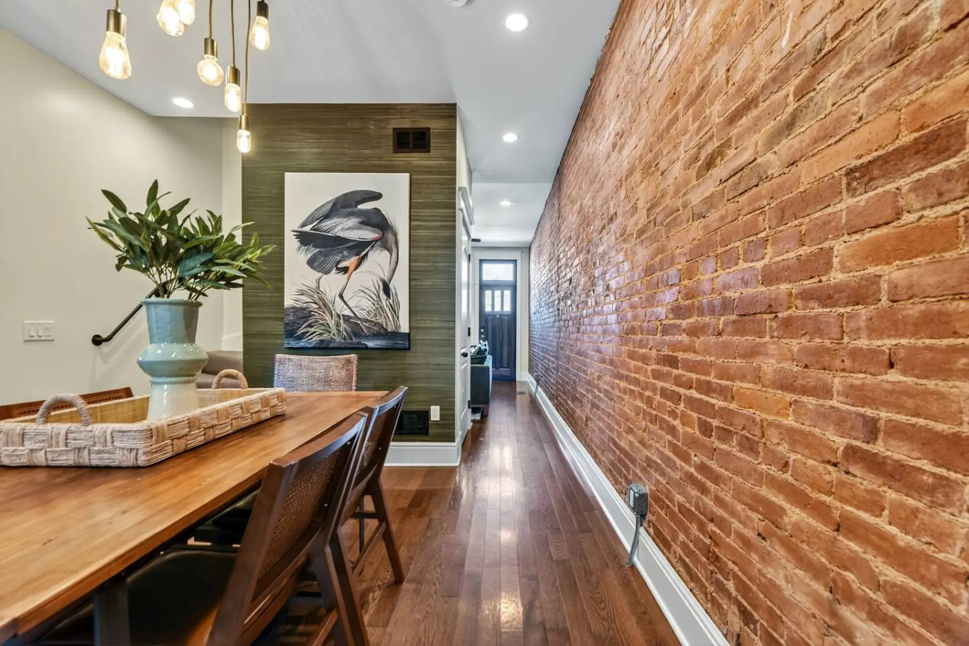 A long, narrow hallway with a brick wall on the right and a dining room on the left.