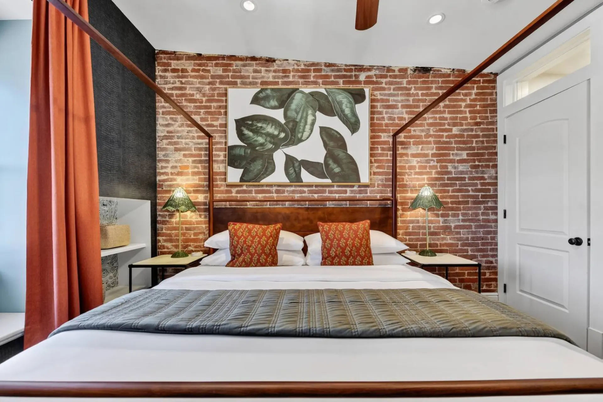 A cozy bedroom with a four-poster bed, brick walls, and orange accents.