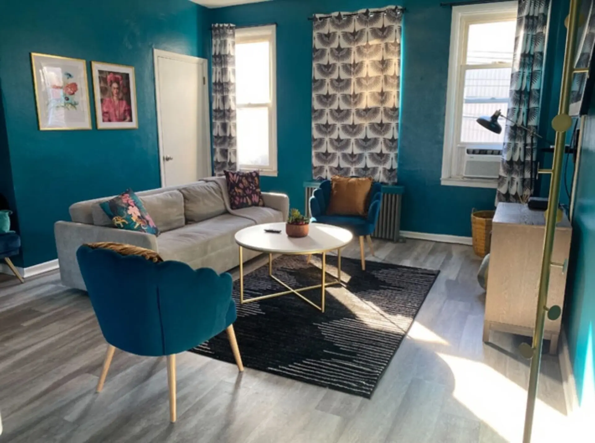 A living room with teal walls, a grey couch, two teal chairs, and a white coffee table.
