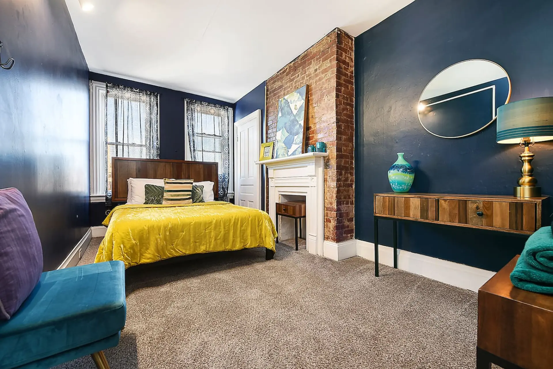 Bedroom with a yellow bed, brick fireplace, dark blue walls, and a gold-framed mirror.