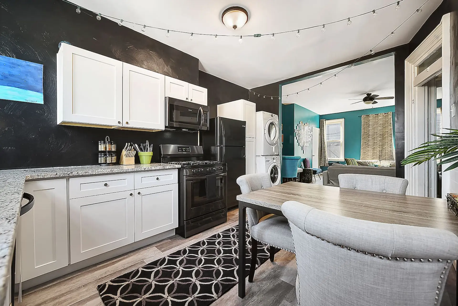 A modern kitchen with black walls, white cabinets, and a dining table.