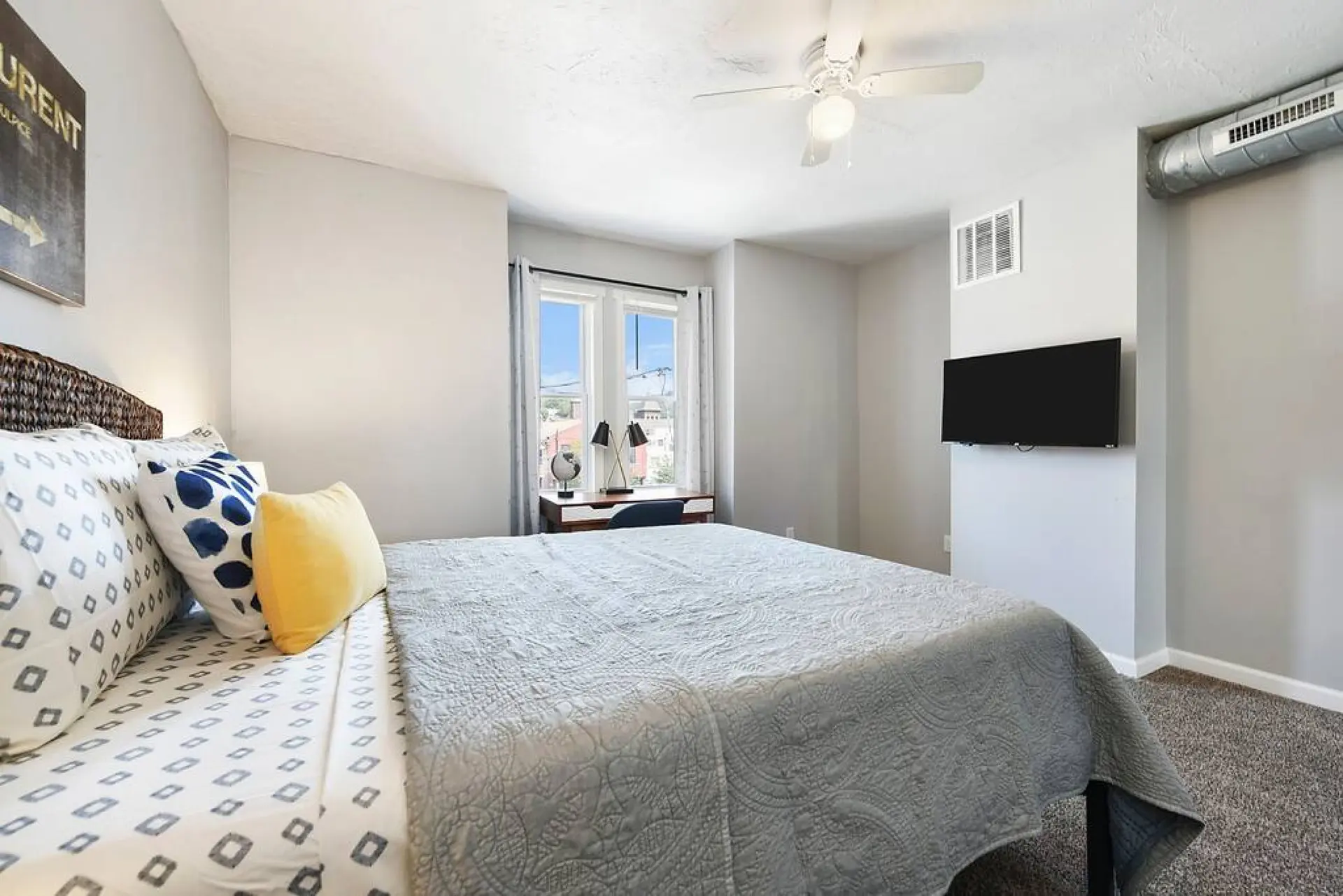 A TV is mounted on the wall above a grey quilted bed.