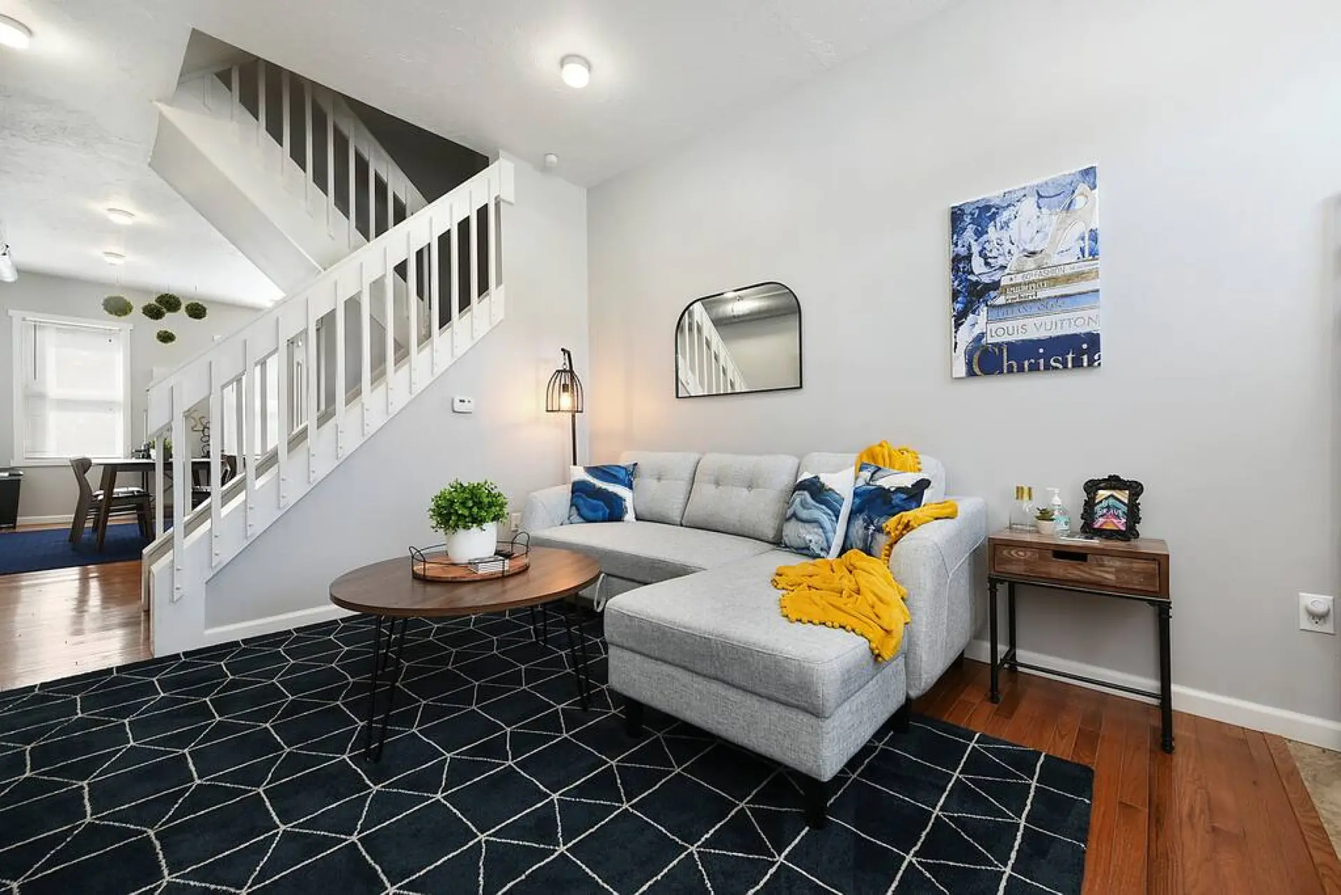 A modern living room with a gray sectional, patterned rug, and a white staircase.
