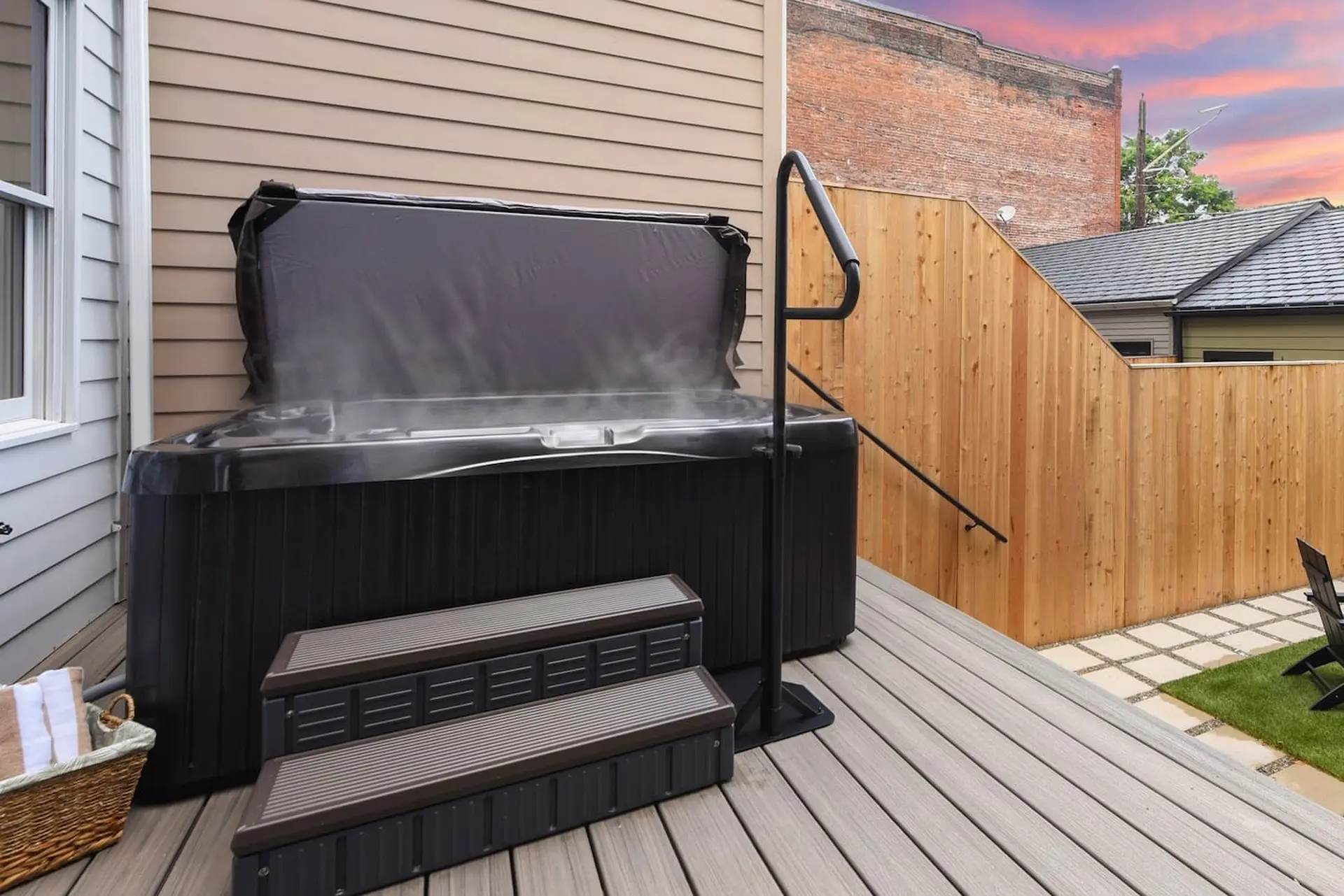 Outdoor hot tub with steam rising from the water, on a wooden deck with steps and a handle.