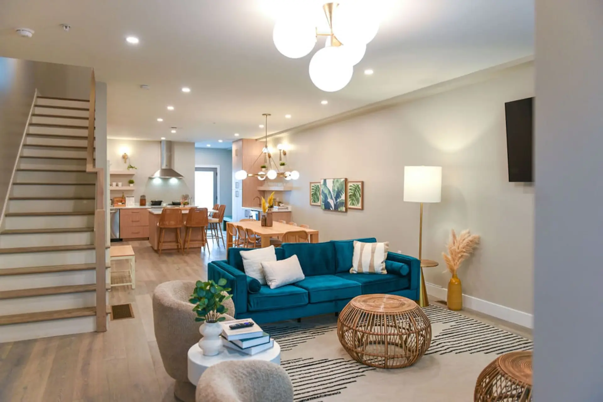 A modern living and dining area with a teal couch, rattan furniture, and light wood floors.