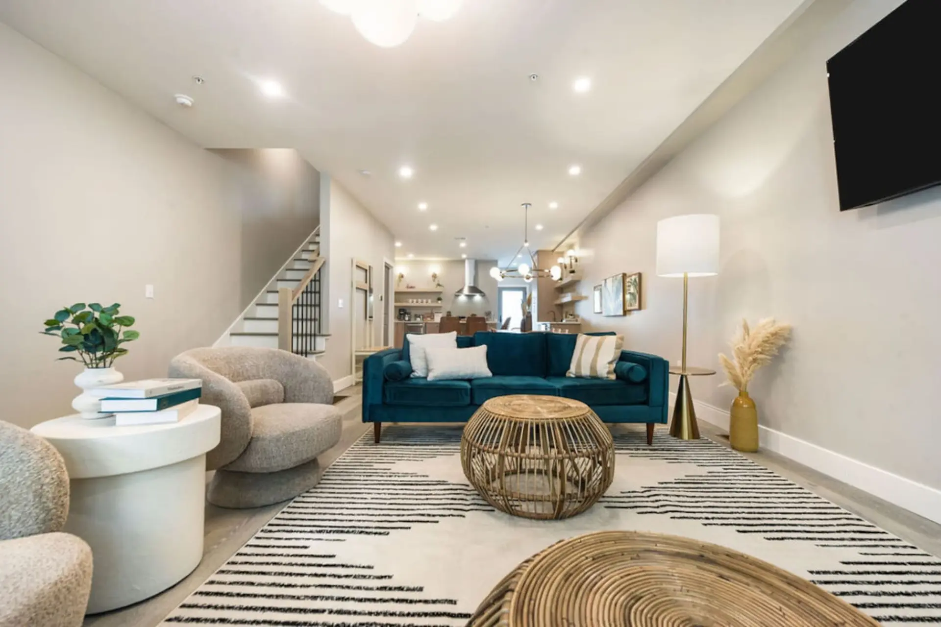 A teal couch is in a well-lit living room with a staircase, a fluffy chair, and a rattan coffee tabl